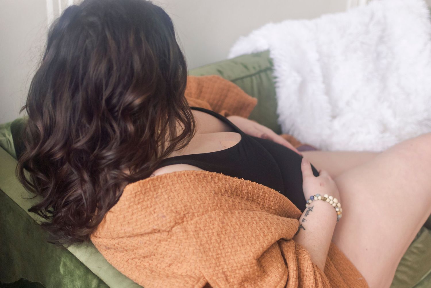 Lifestyle portrait of a pregnant woman sitting on a couch in a curated, natural light photography studios in Hartford, CT