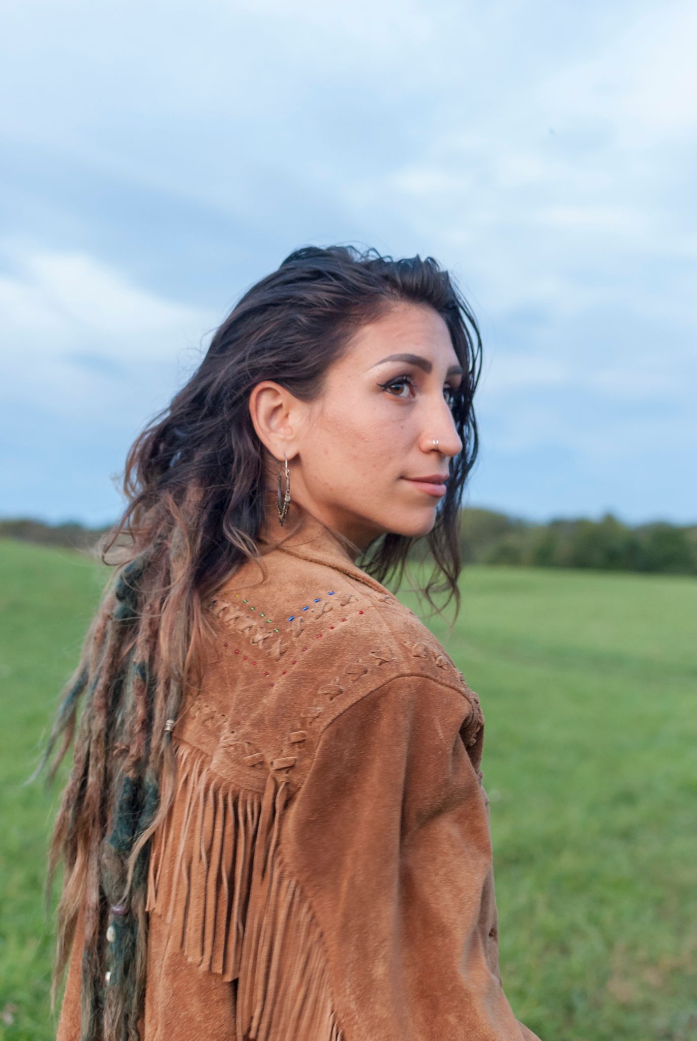 Lifestyle portrait of a young women with dreadlocks in a field