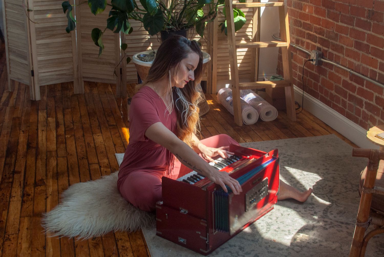 Lifestyle Portrait of young woman playing kirtan harmonium in sun lit apartment for branding photography