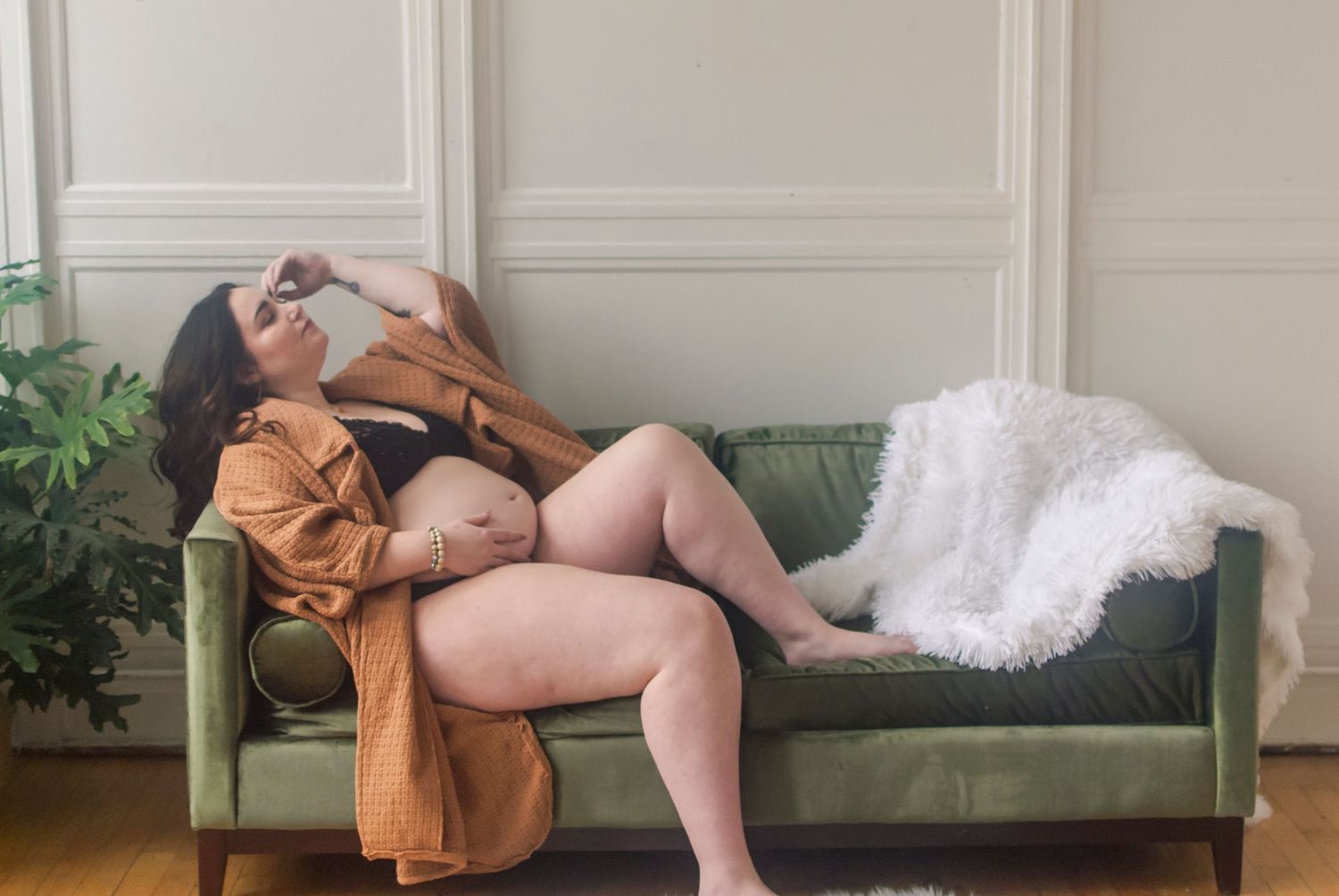 Lifestyle portrait of a pregnant woman sitting on a couch in a curated, natural light photography studios in Hartford, CT