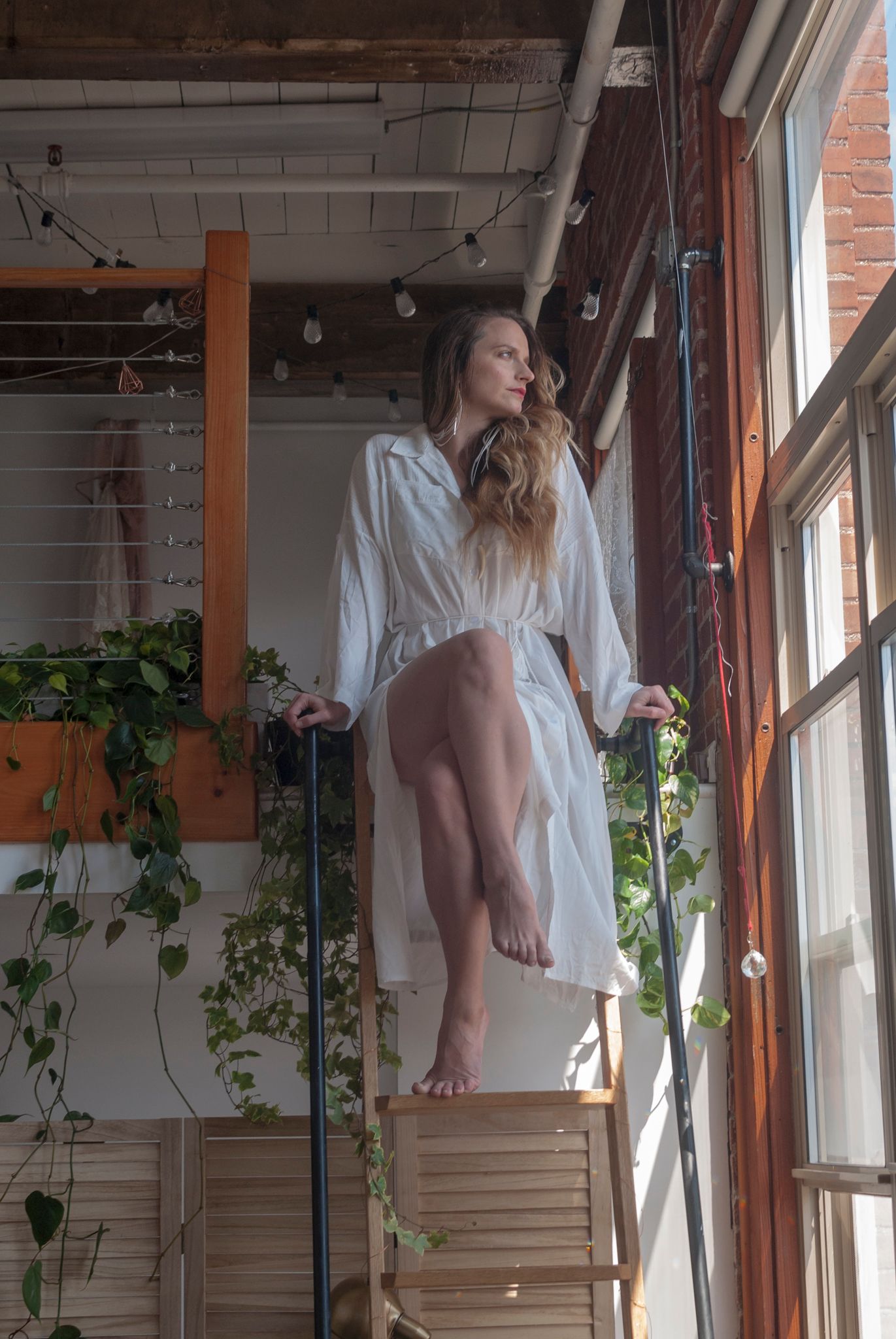 Portrait of a young woman in a white dress in a sunlit studio loft
