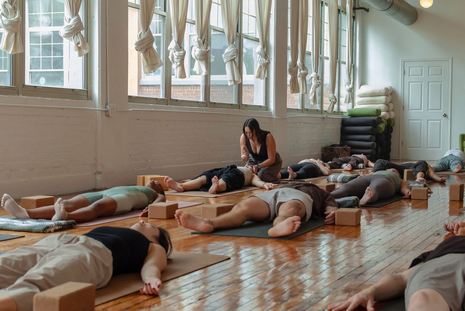 Yoga teacher assisting a student in savasana in a full yoga class setting in Hartford, CT