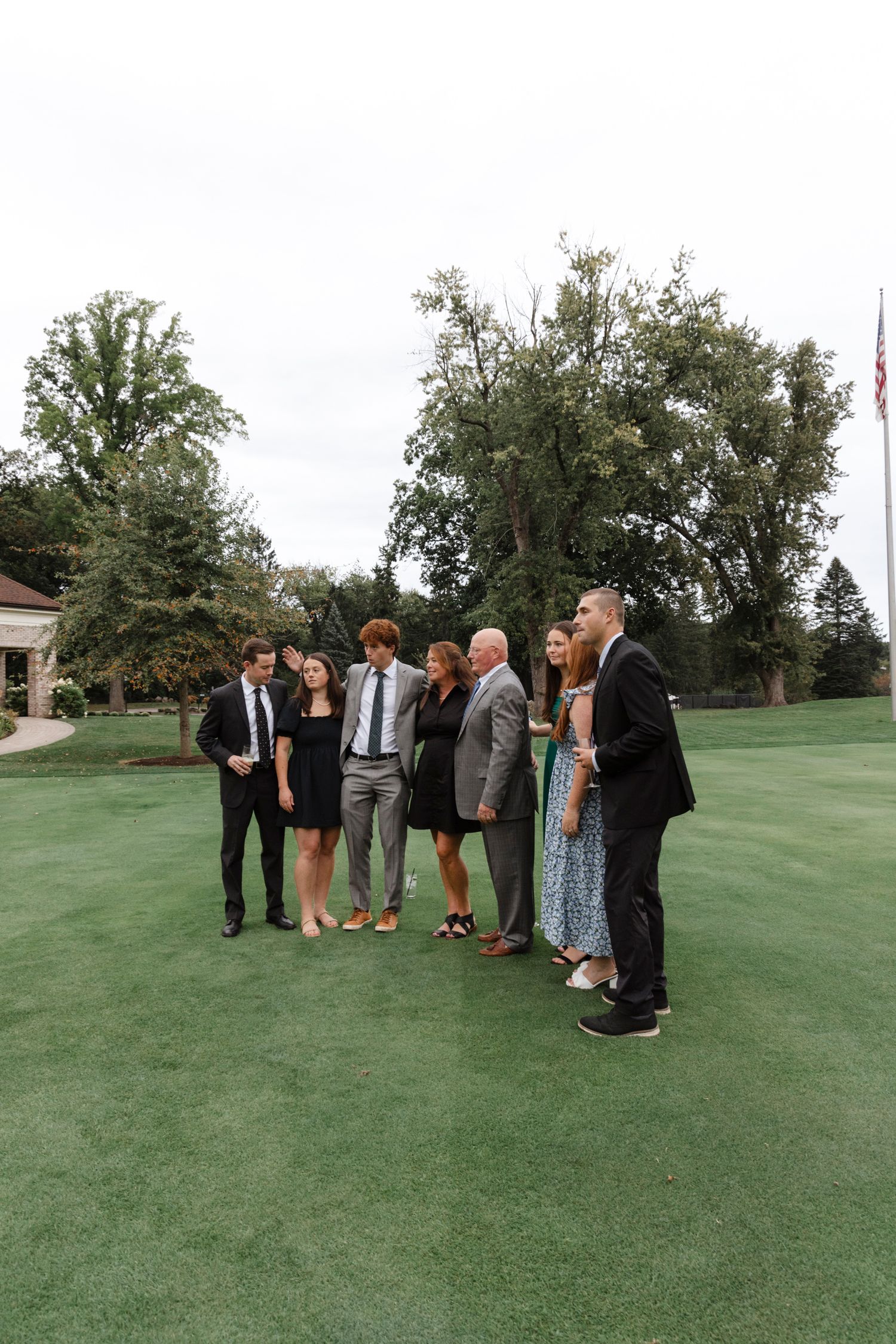 Wedding guests gathered on a lush green lawn with trees in the background. Rochester NY documentary wedding photography