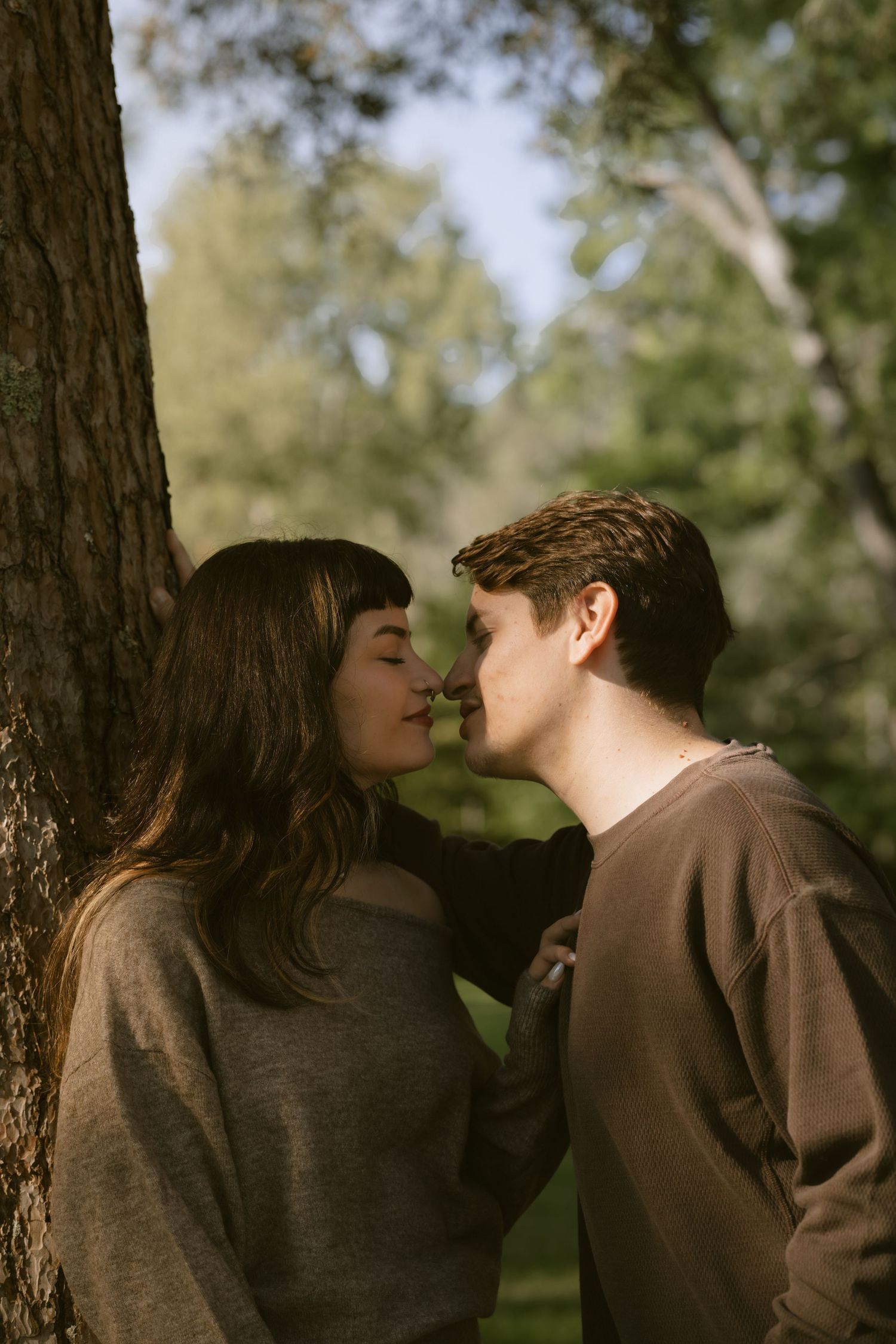 A tender moment between a couple among tall trees in warm forest lighting.  Rochester NY film engagement photography