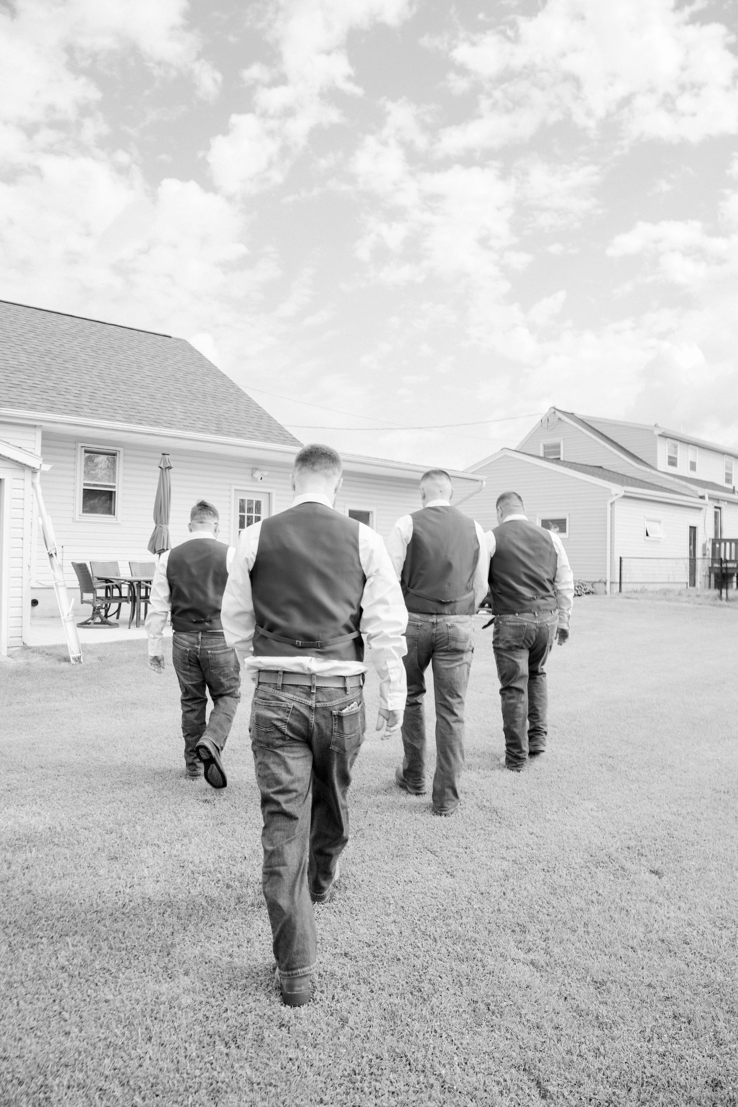 A group walks across a grassy field towards white buildings in black and white.  Camp Brockway Wedding photographer