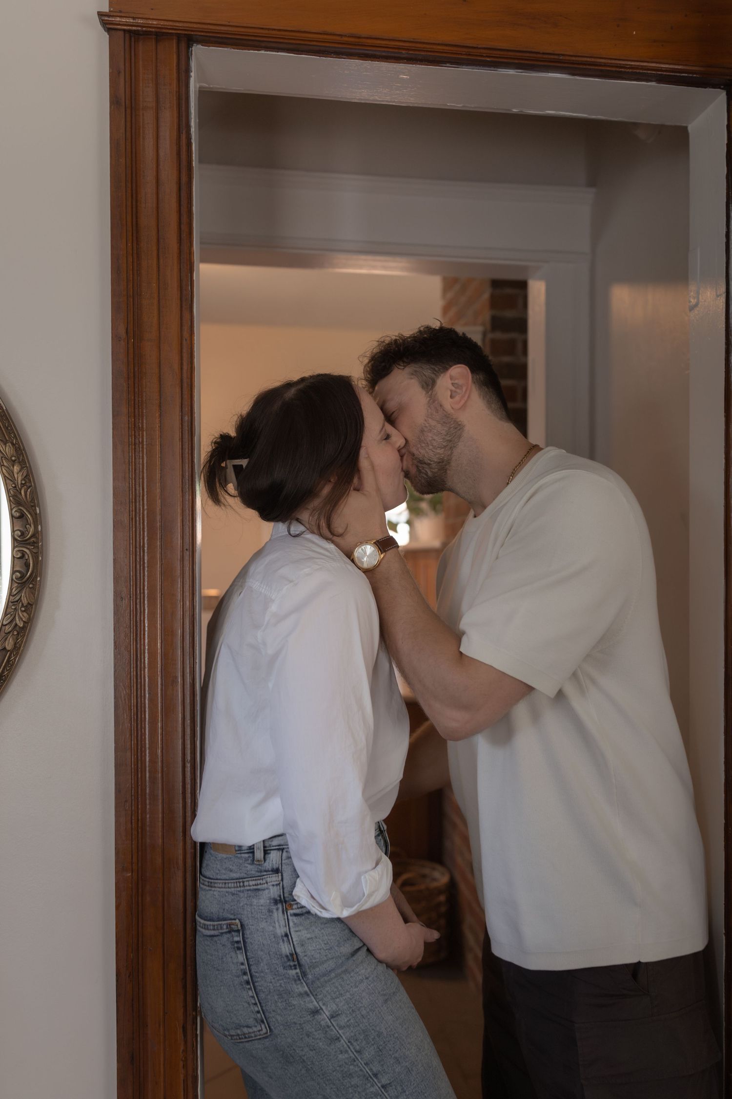 Couple sharing a tender kiss in a doorway, man gently holding woman's face, both in casual white and denim outfits.
