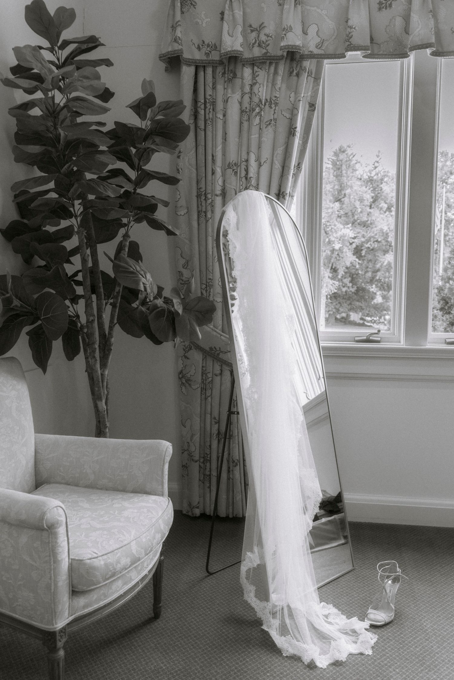 Wedding dress hanging by window with elegant curtains and indoor plants.Rochester NY documentary wedding photographer