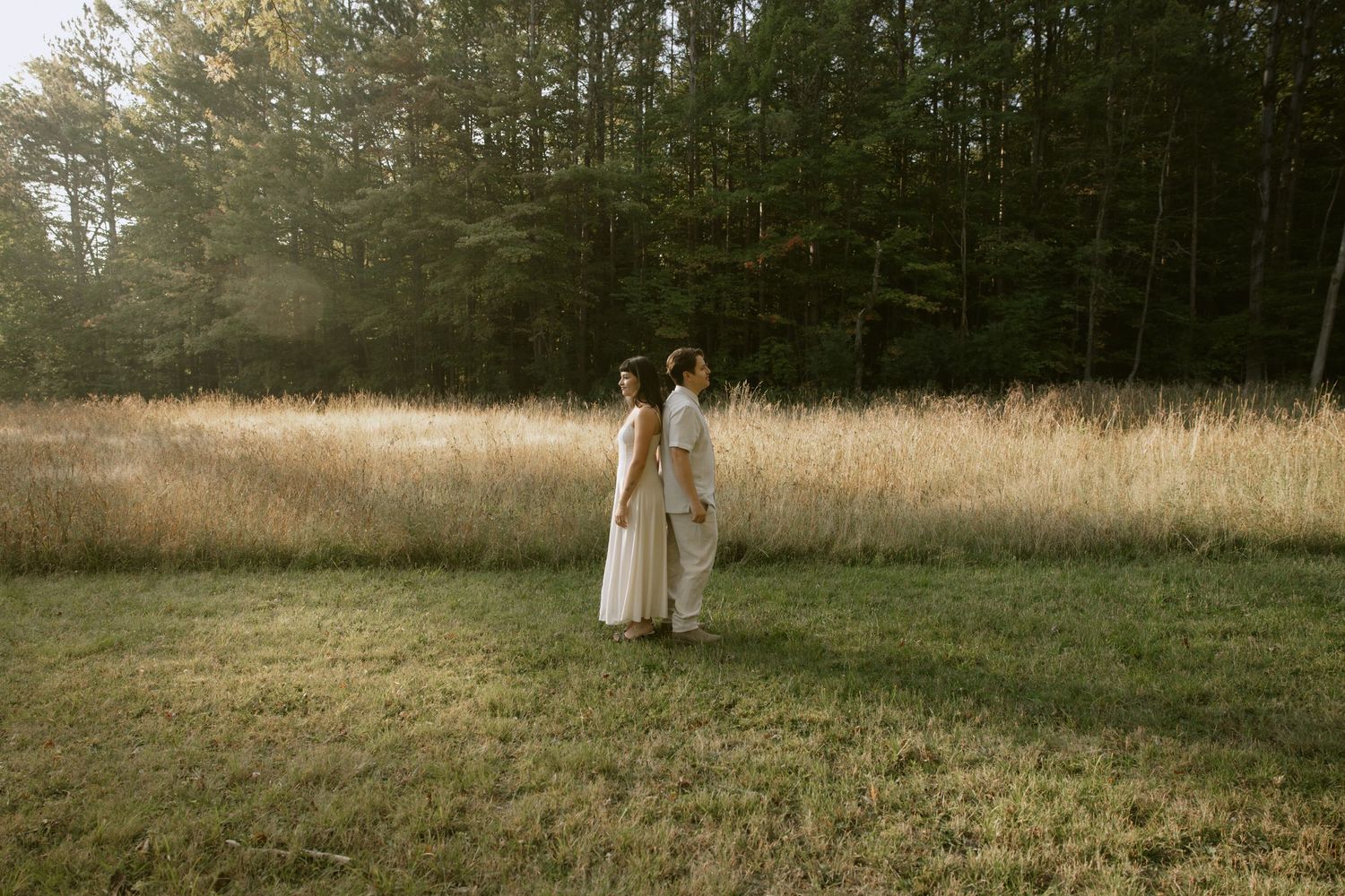 Wide landscape shot of people walking through a grassy field near a forest. Rochester NY authentic engagement photography