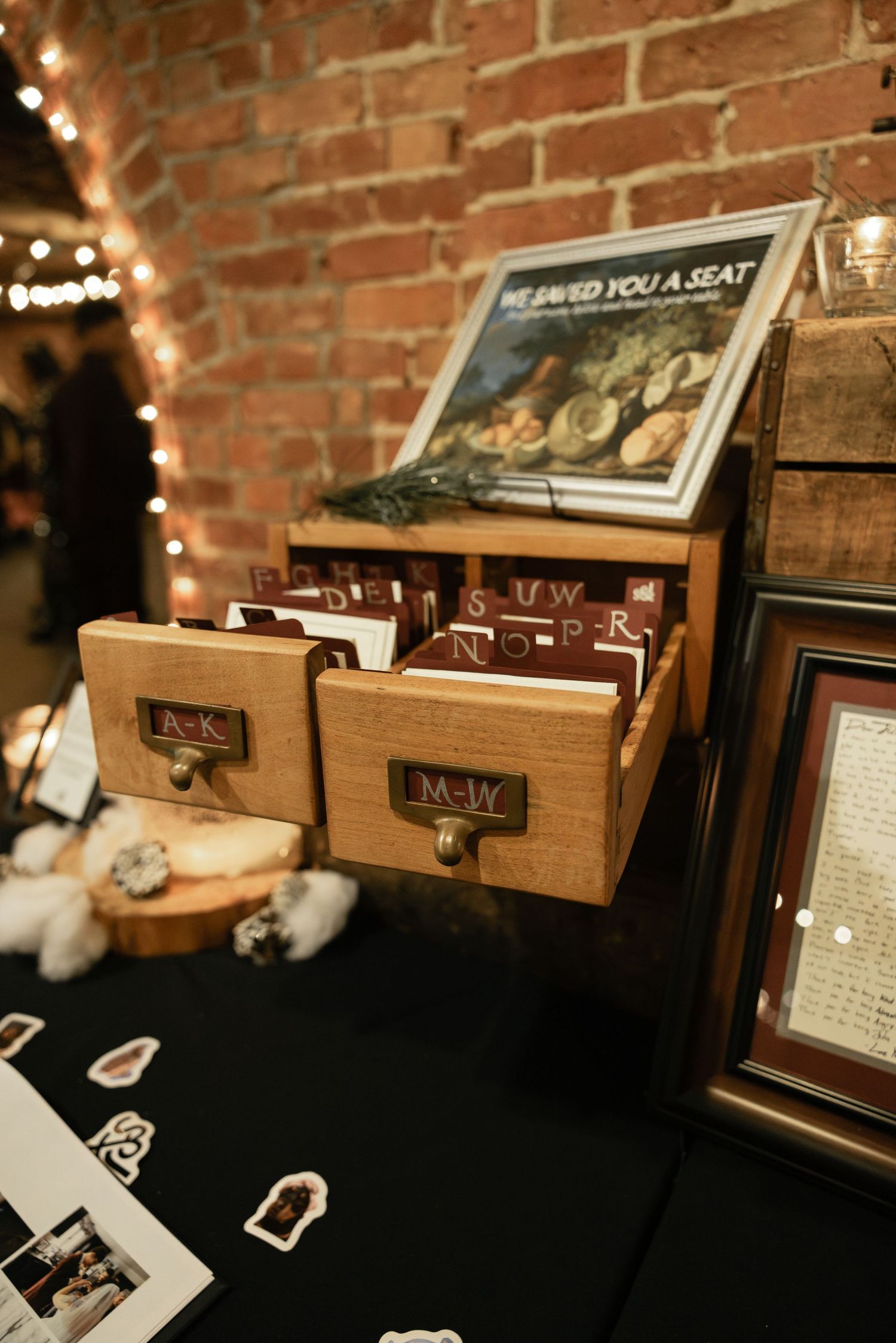 A vintage-style wooden cabinet with drawers and a display case showcasing various items, set against a brick wall with string lights.