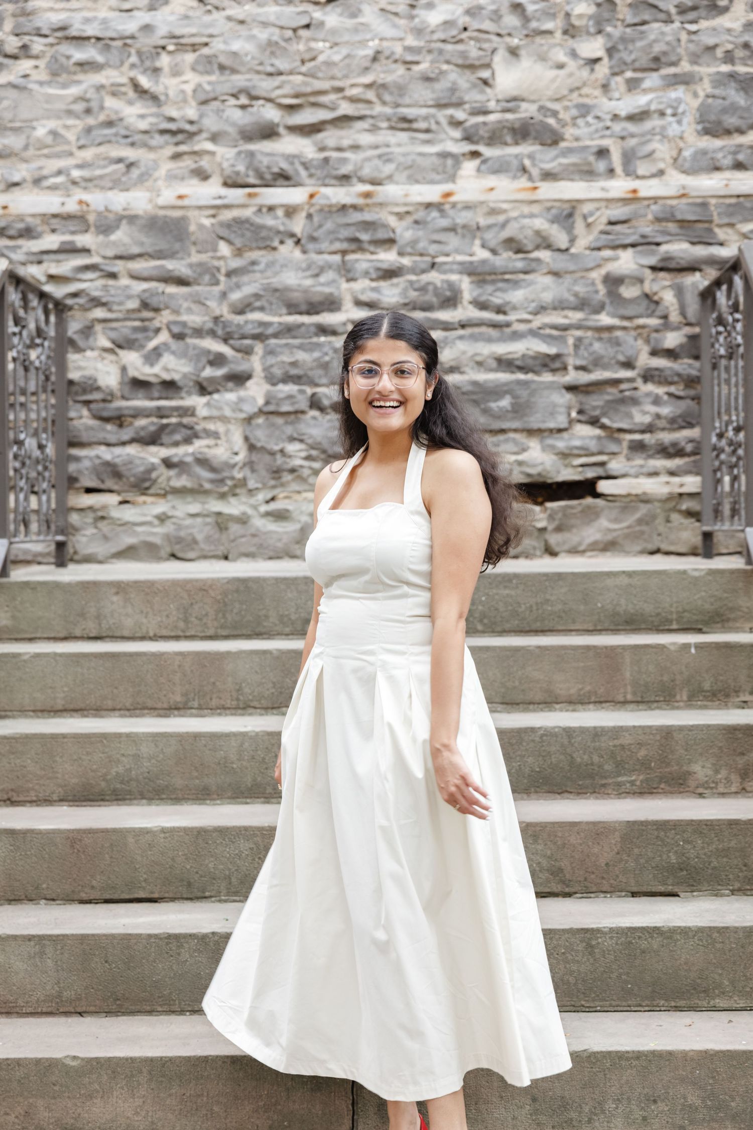 A person in a white halter dress poses joyfully on stone steps against a textured wall.  St. Josephs park wedding photographer