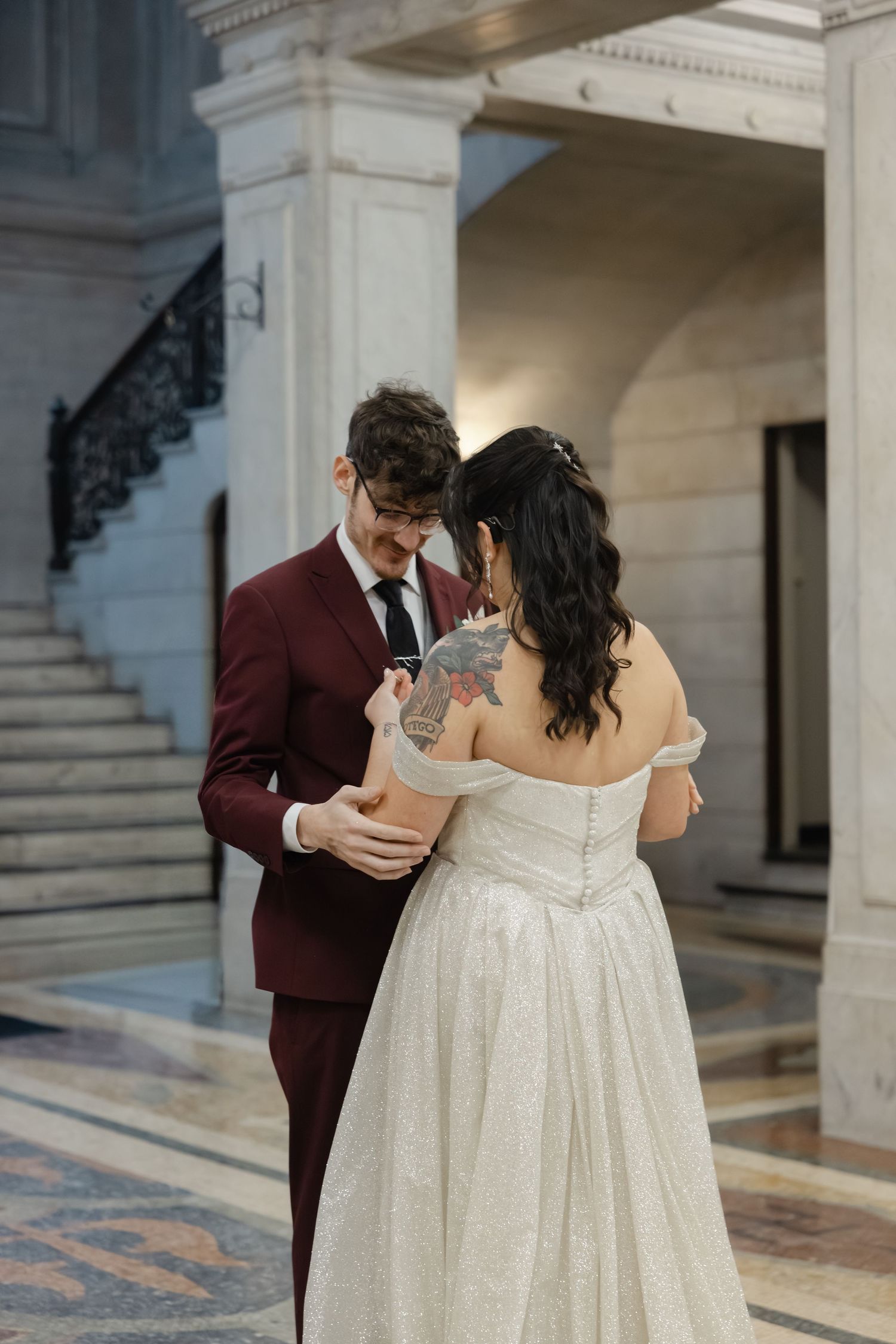A bride and groom in formal attire embrace on a marble floor in an ornate interior setting.