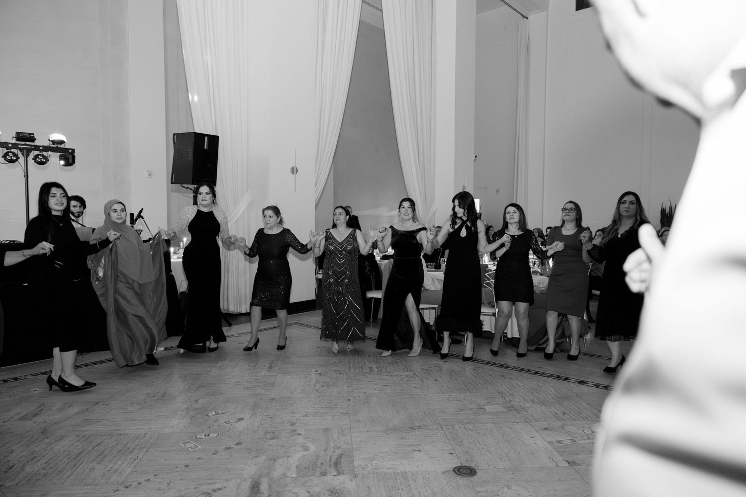Large group of wedding guests forming a line dance at a reception with white draped walls. Rochester NY film wedding photographer