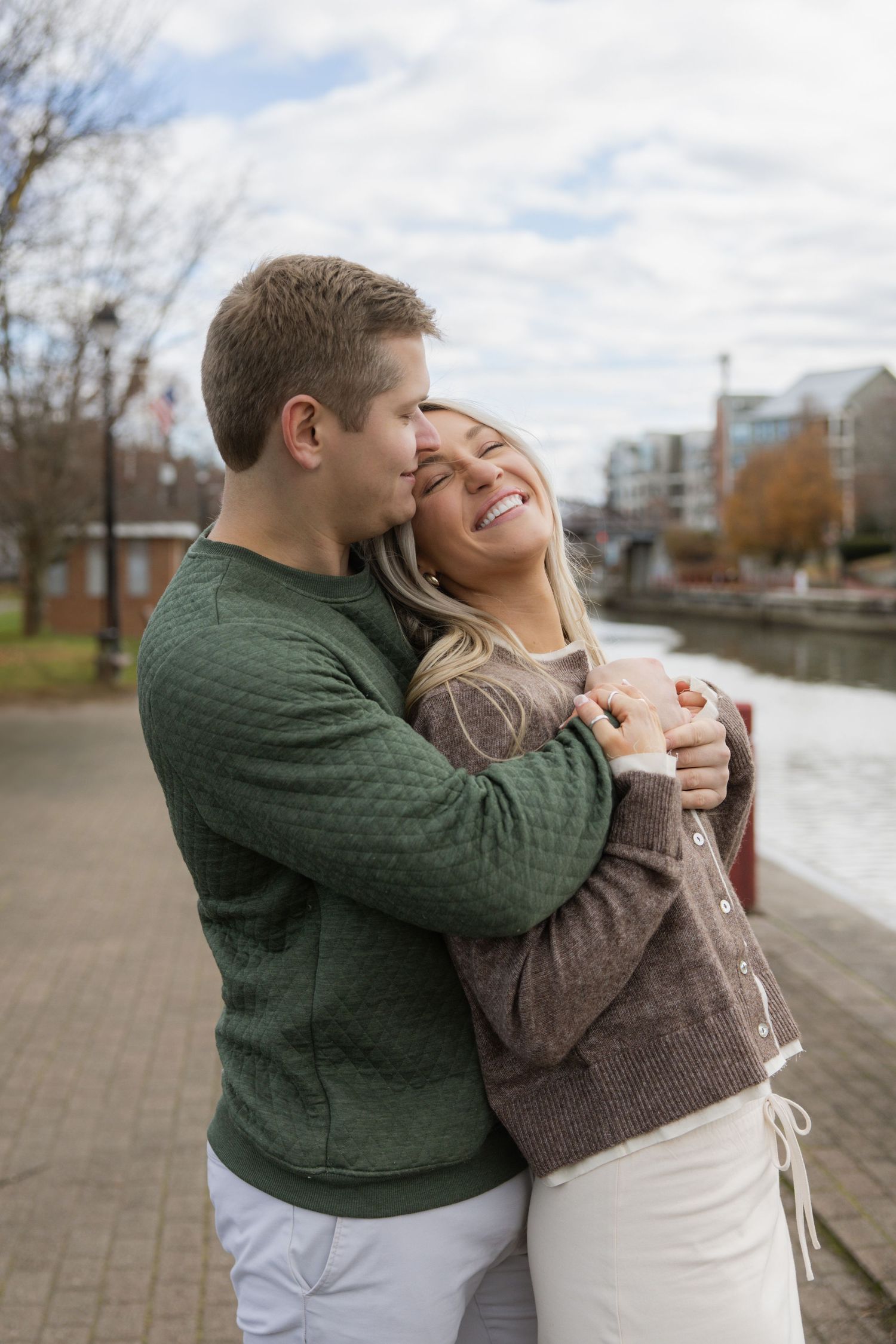 A couple shares a joyful embrace while standing on a riverside walkway on an autumn day. Film wedding photographer Rochester  NY