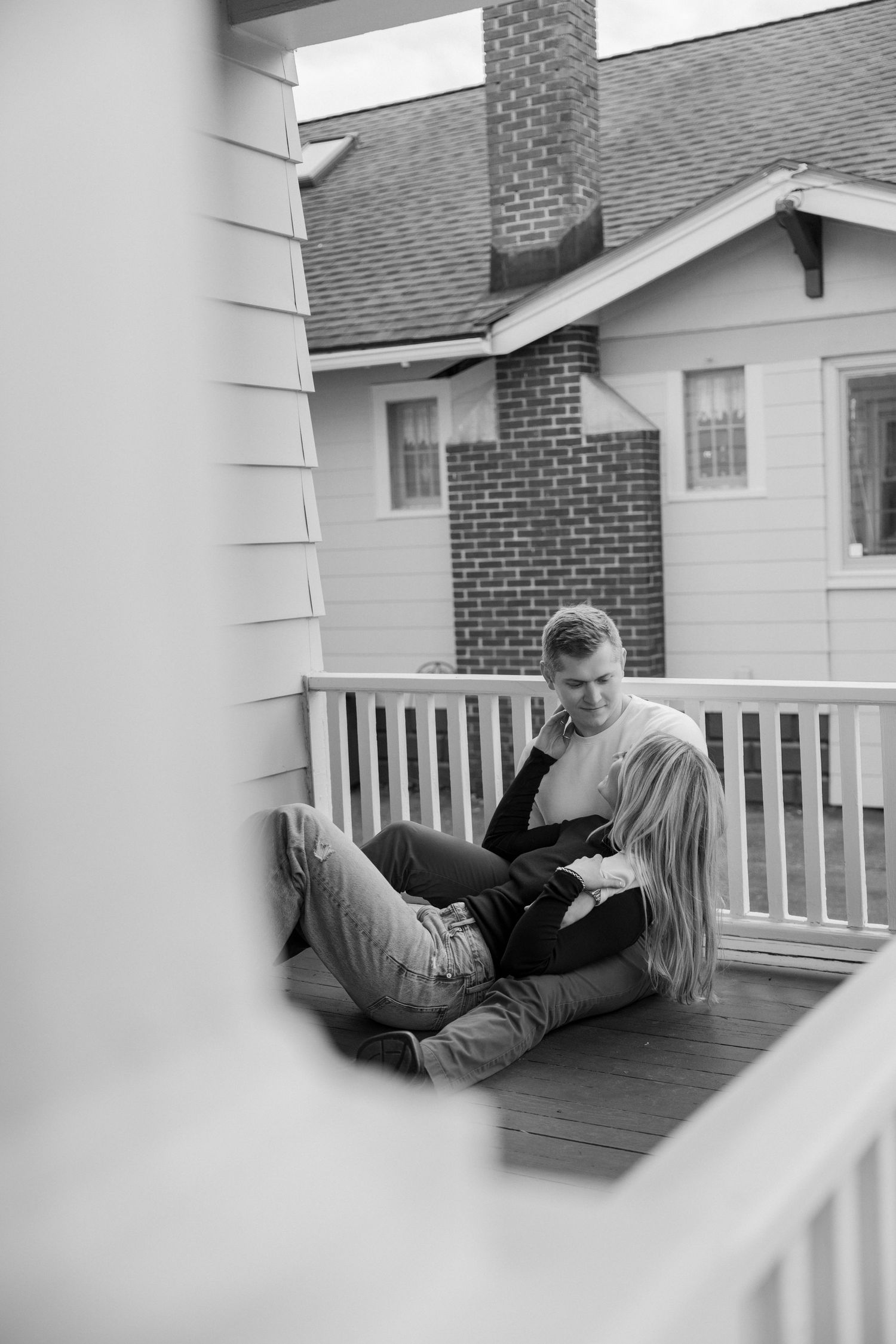 Black and white photo of a couple lounging on their porch. Rochester NY home engagement photography