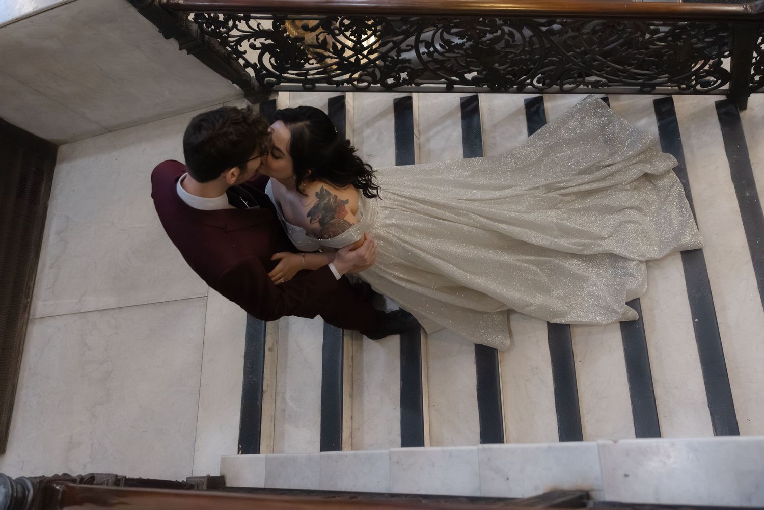 Overhead view of a couple in wedding attire embracing on white and black striped stairs.