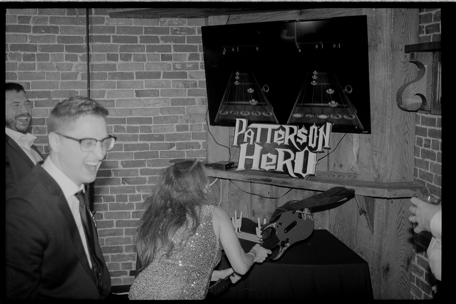 A vintage black and white photo showing people gathered around a sign that reads 'Patterson Here' against a brick wall.