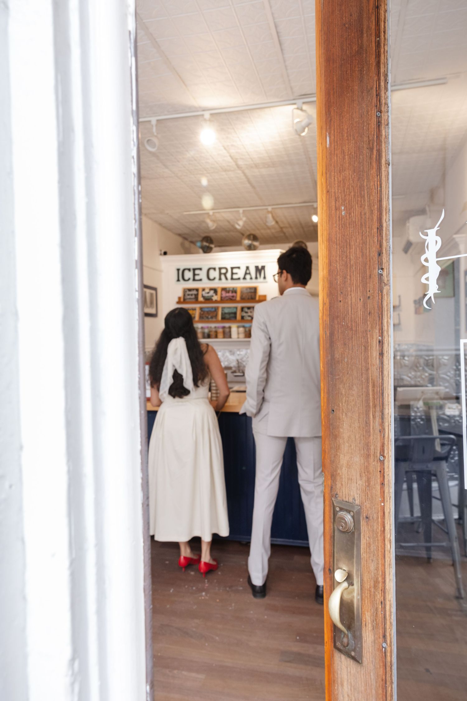 A couple enters an ice cream shop together, with the person in red shoes wearing a white dress.  Fun elopement photography Rochester NY