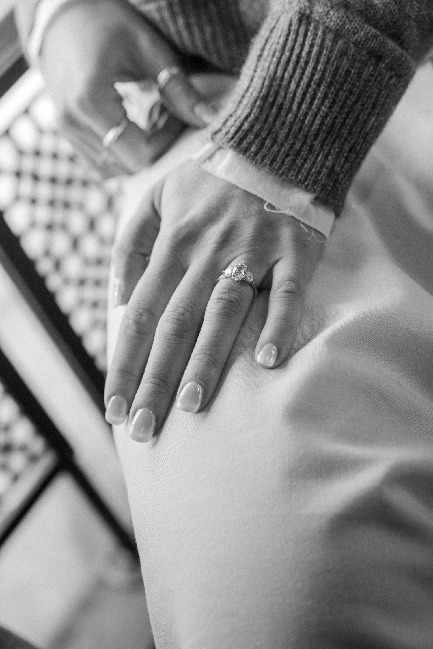 Close-up black and white photo of an engagement ring on a woman's hand with a sweater sleeve.