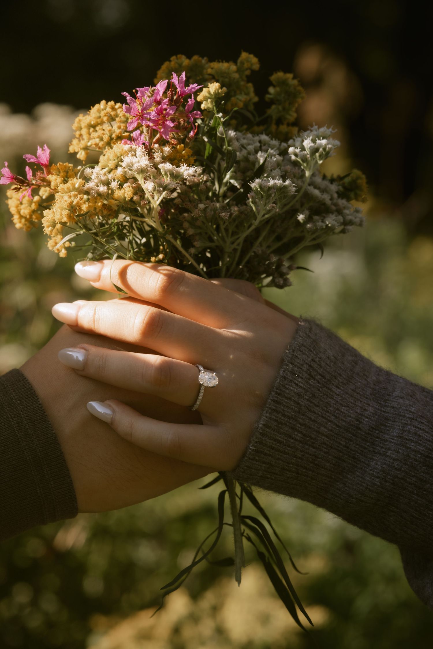 Hands holding a delicate bouquet of dried flowers with an engagement ring visible. Rochester NY documentary engagement photography