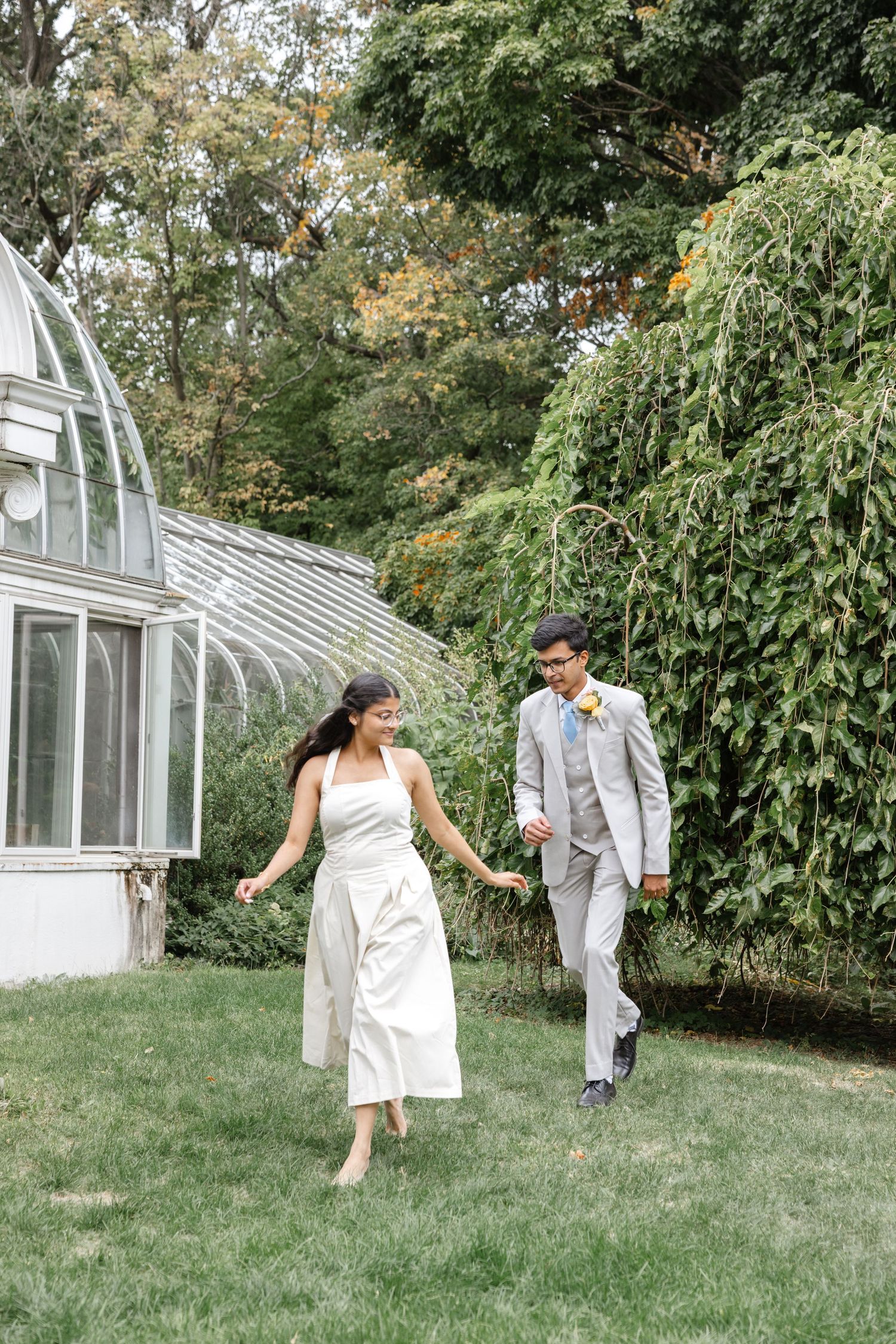 Playful dance sequence on a grassy lawn with a greenhouse in the background. Rochester conservatory wedding photographer