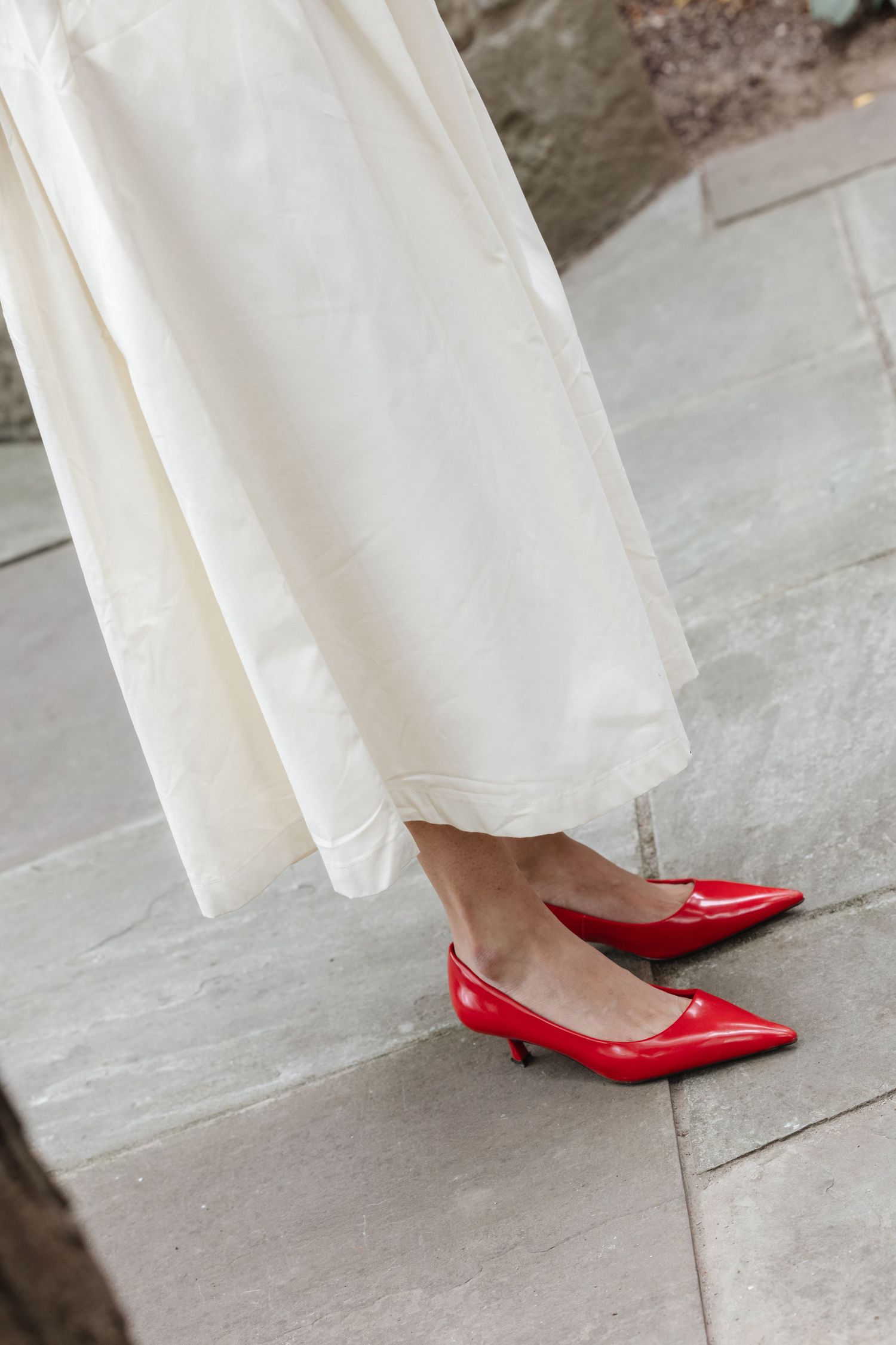 Woman wearing white dress and bright red pointed-toe flats on stone floor.  St. Josephs park wedding photographer