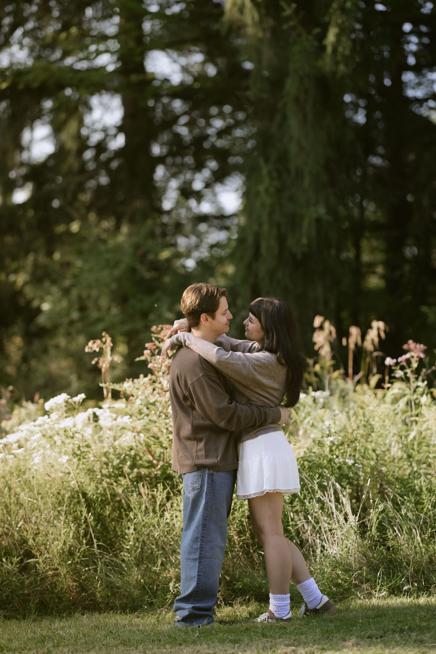 Two people embrace while standing in a field of wildflowers and tall grass. Rochester NY film engagement photography