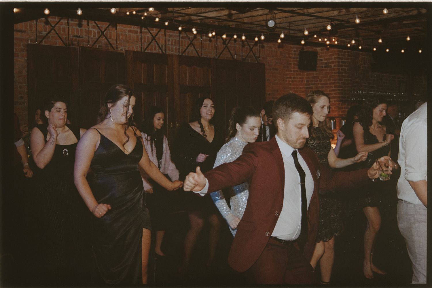 A group of people dancing at a lively social event, with string lights illuminating the scene.