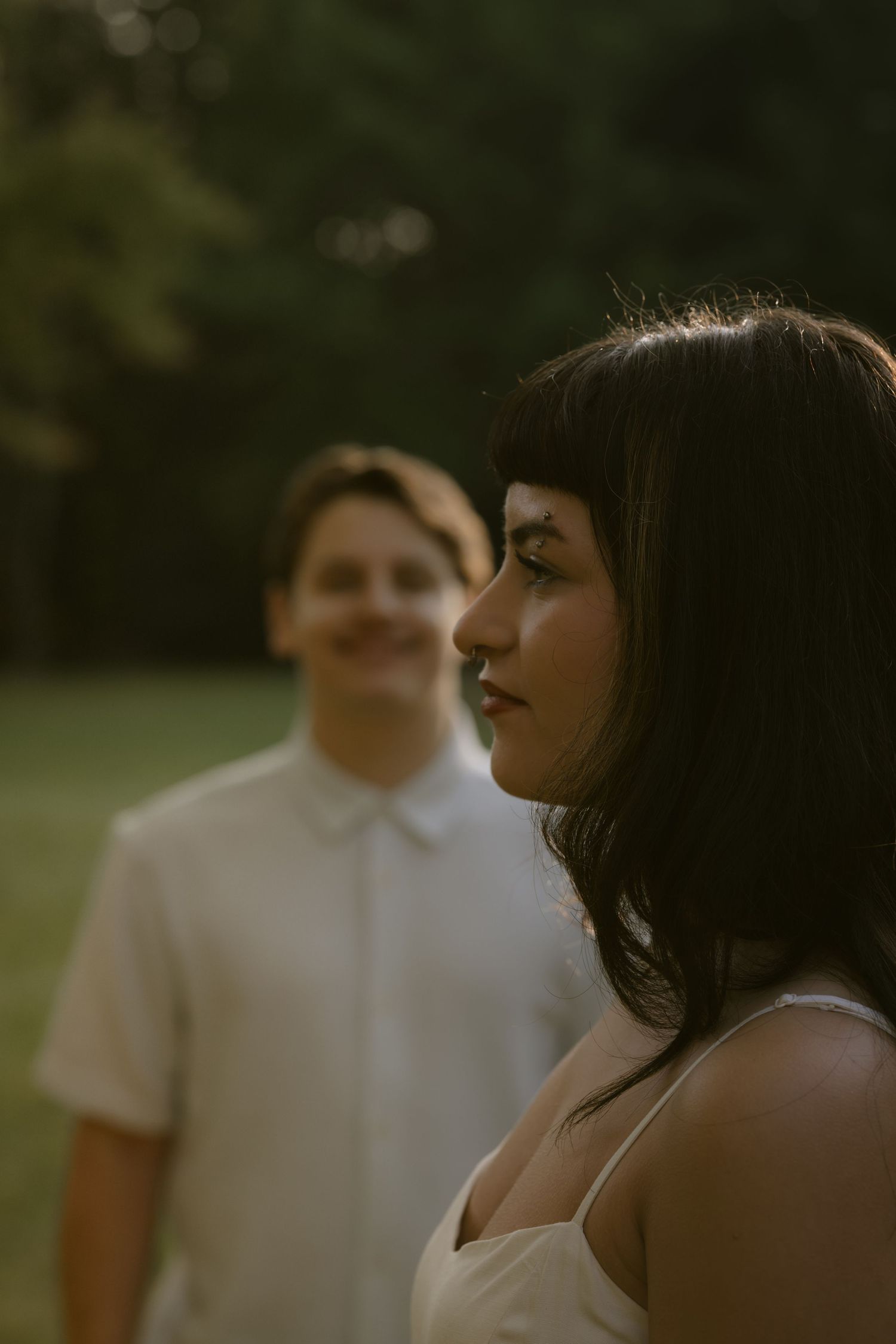 Two people in white clothing pose together during golden hour in a natural setting. Rochester NY authentic engagement photography