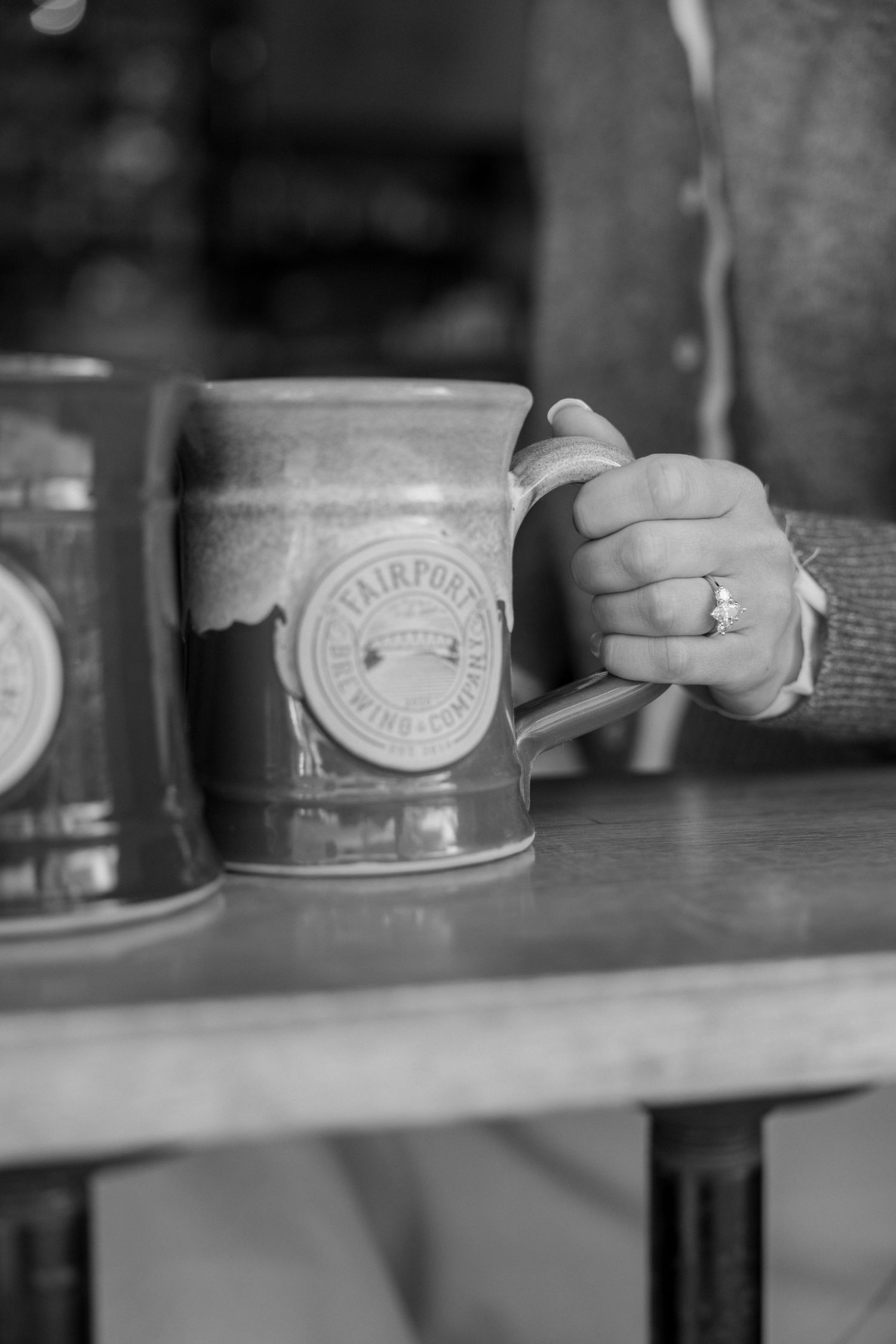 Black and white close-up of coffee mugs being held on a wooden surface.