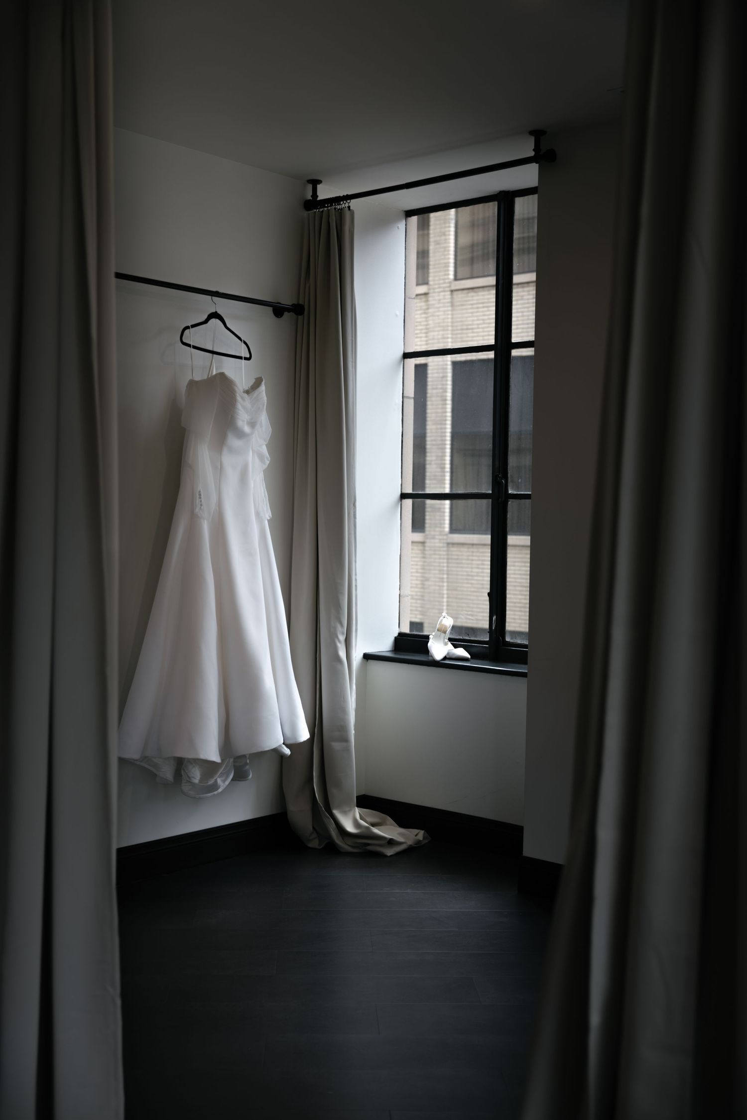 Wedding dress hanging in minimalist room with window and curtains.