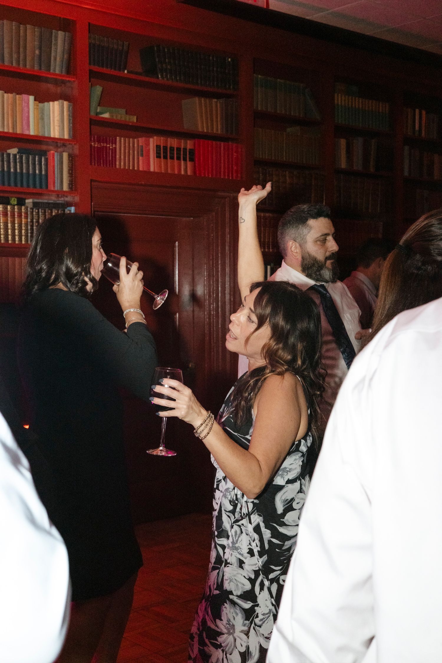 People dancing and celebrating in a room with red-lit bookshelves. Rochester NY documentary wedding photography