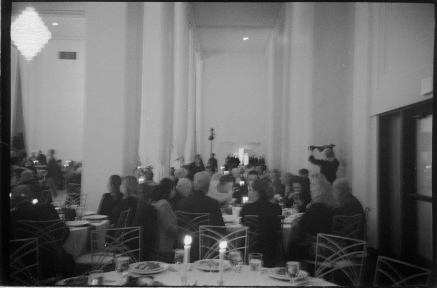 Black and white photo of a formal event space with guests gathered in the background. Rochester NY film wedding photographer