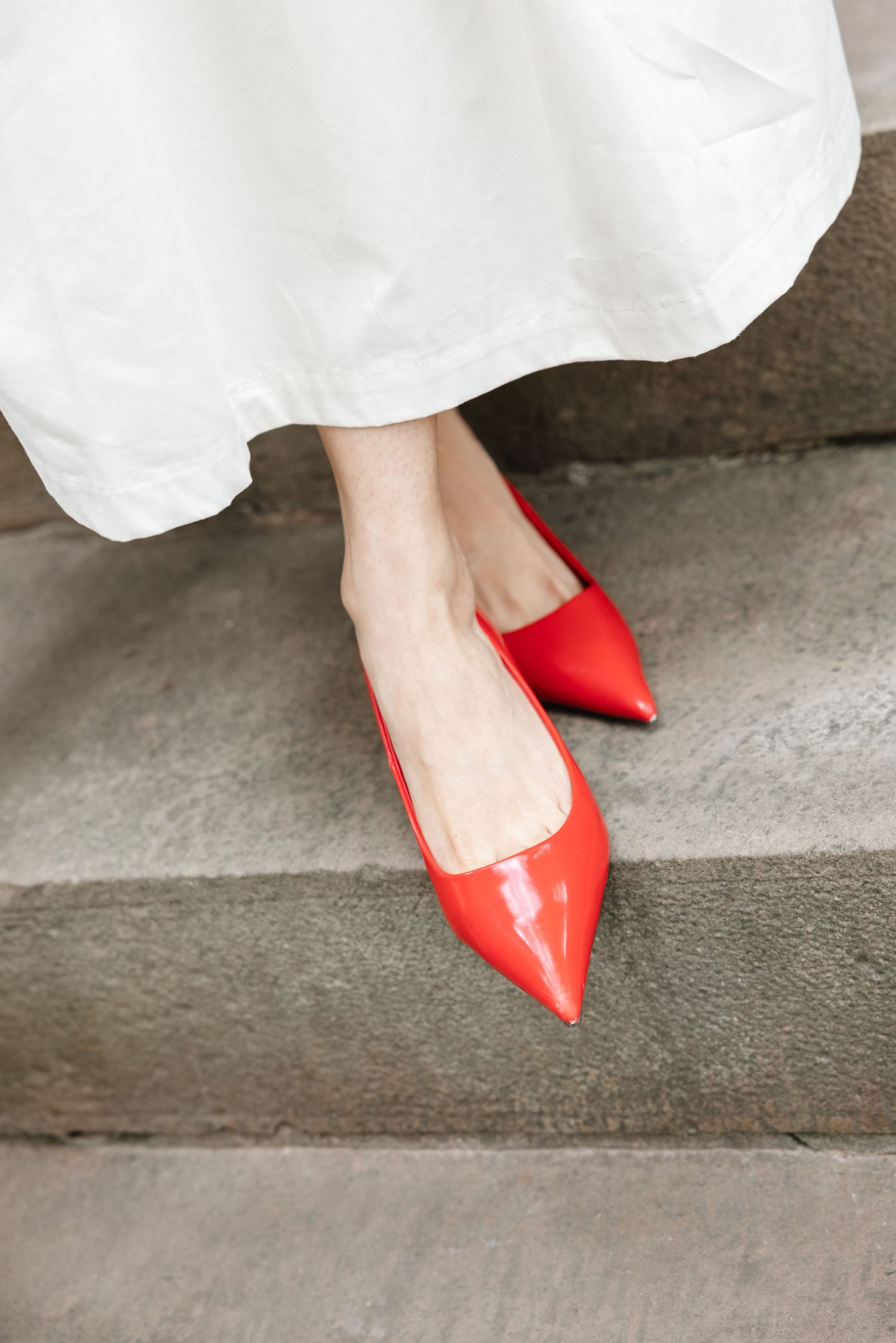 Close-up of bright red pointed flats against a white dress hem on concrete steps.  St. Josephs park wedding photographer
