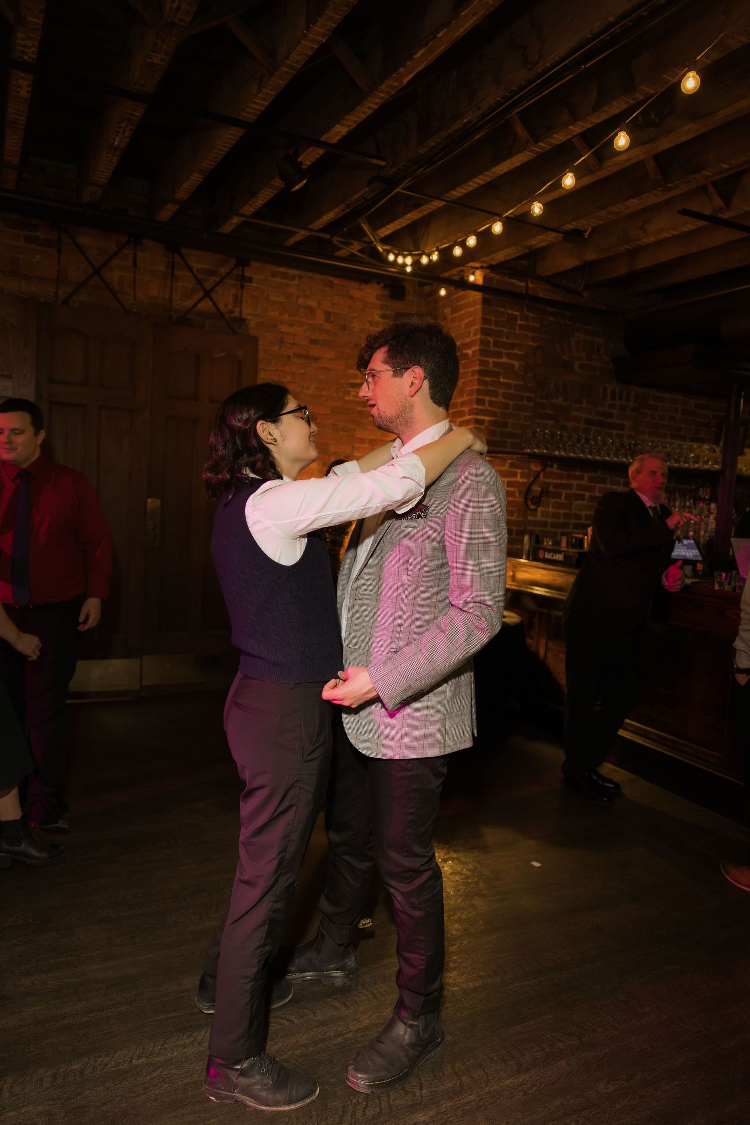 Two people are dancing together in a dimly lit room with string lights hanging from the ceiling.