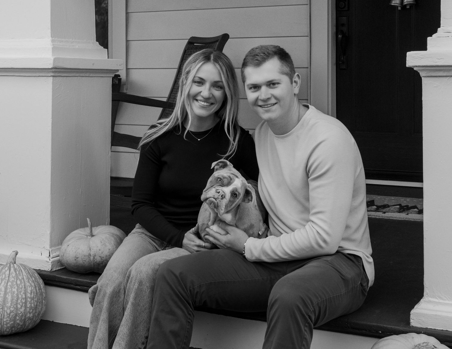 A couple sharing tender moments on a white porch with classic architecture. Fairport NY home engagement photography