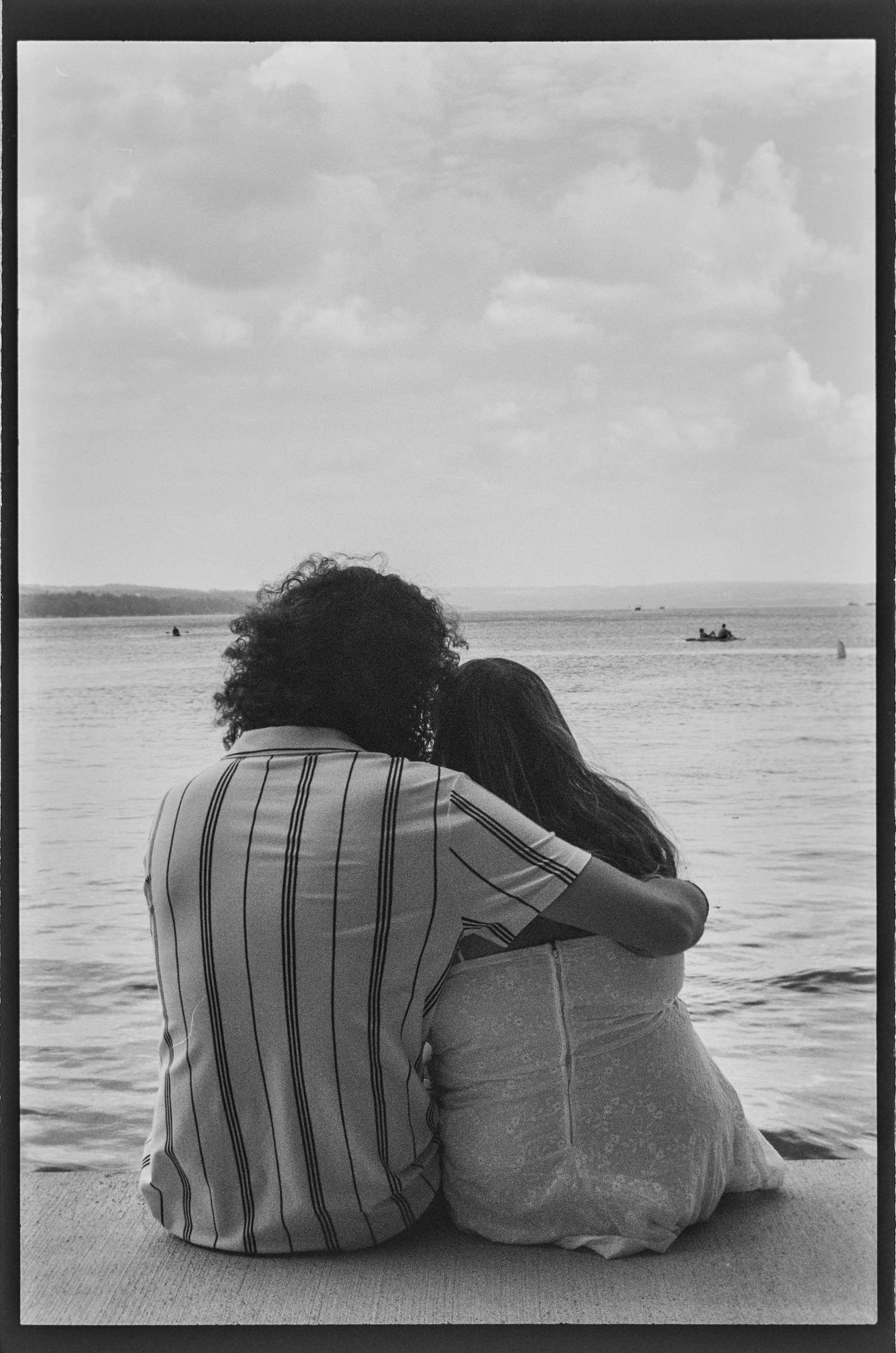 A black and white photo of two people sitting close together by the ocean. wedding photographer Syracuse