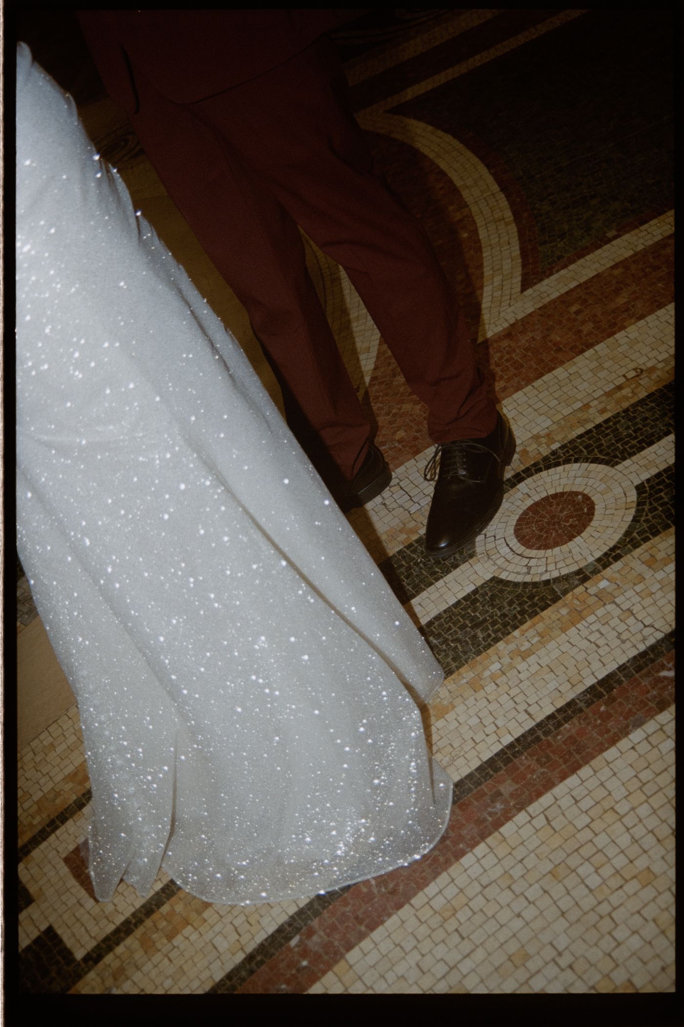 The image shows a white wedding dress on the floor of a tiled bathroom, with a dark background and a decorative design on the tiles.