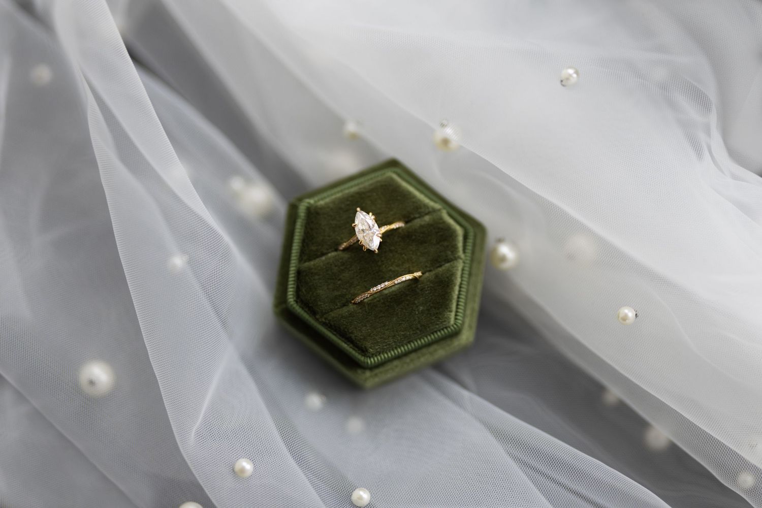 Wedding ring displayed in a green velvet hexagonal box on delicate tulle fabric.
