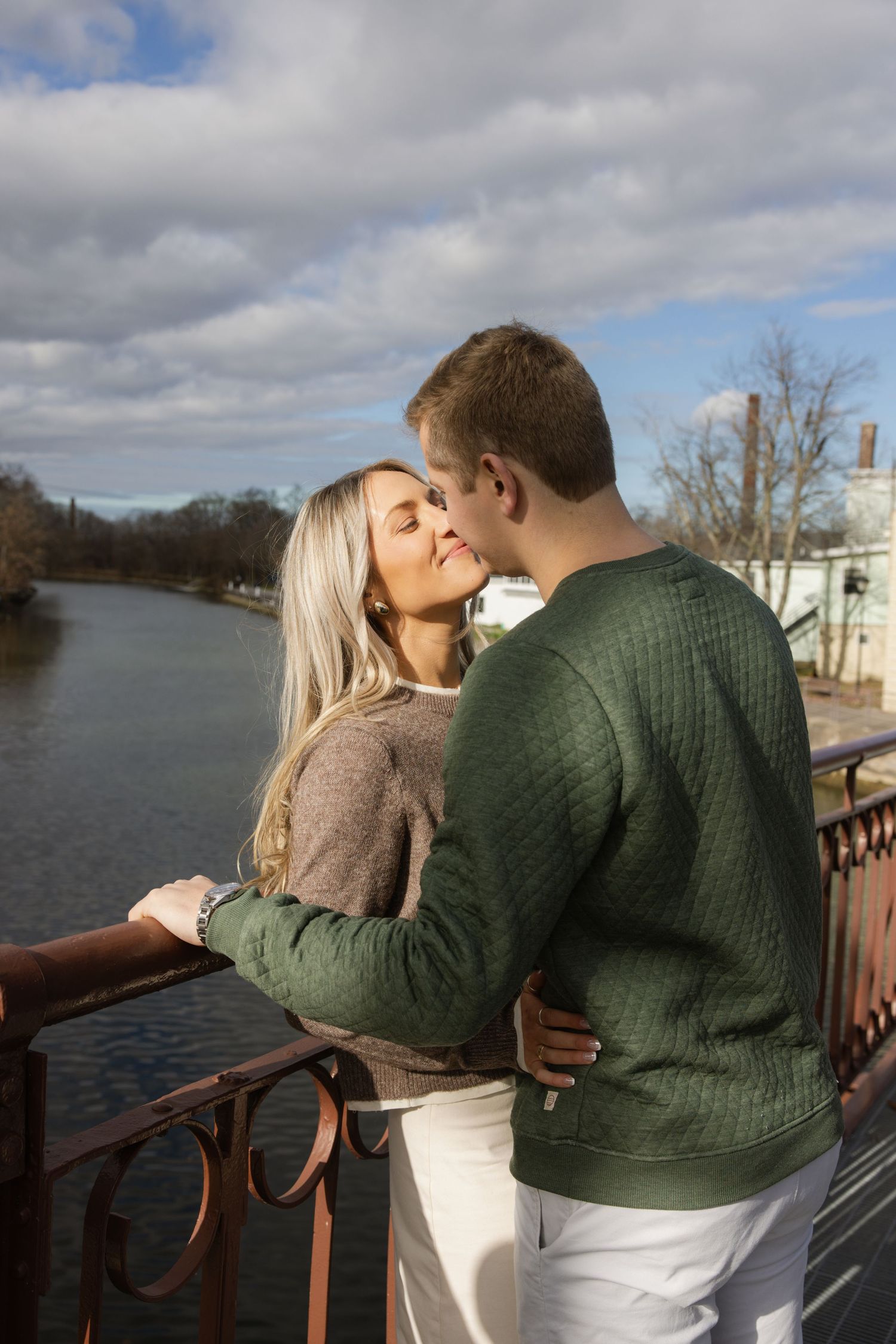 A couple embraces while sharing a tender moment on a bridge overlooking a river on a cloudy day. Film wedding photographer Rochester  NY