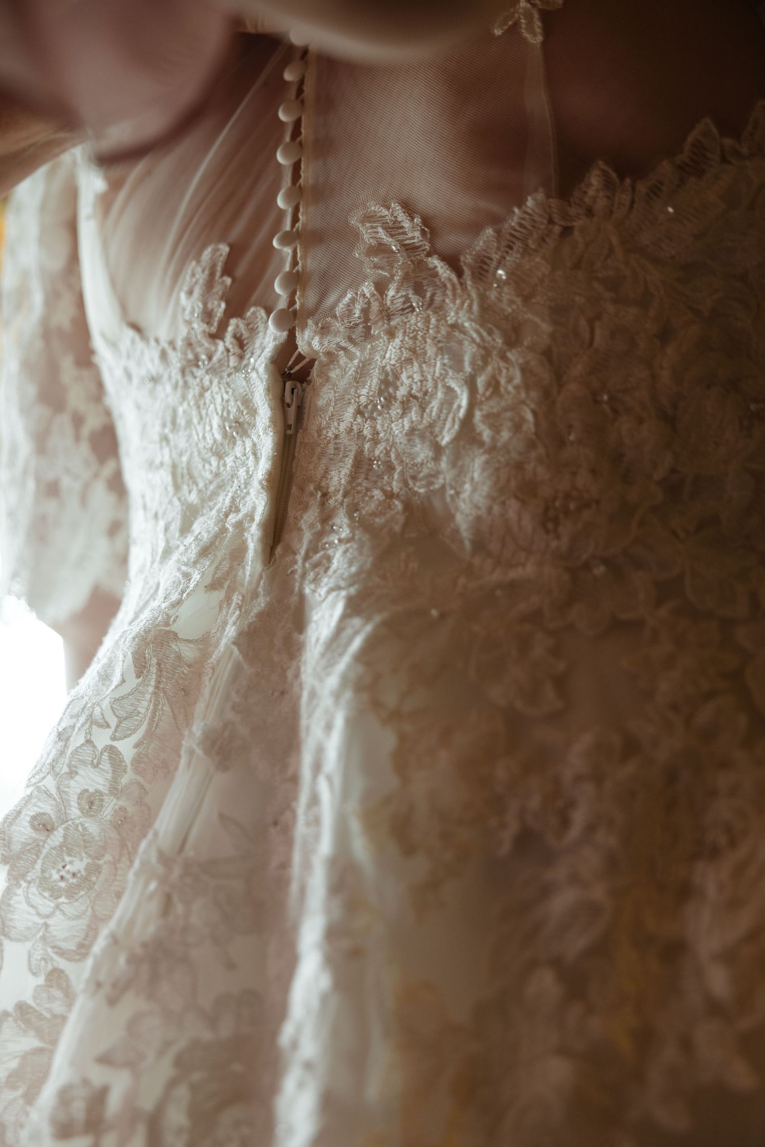 Close-up detail of ivory wedding dress lace showing intricate embroidered patterns. Documentary wedding photographer Syracuse NY