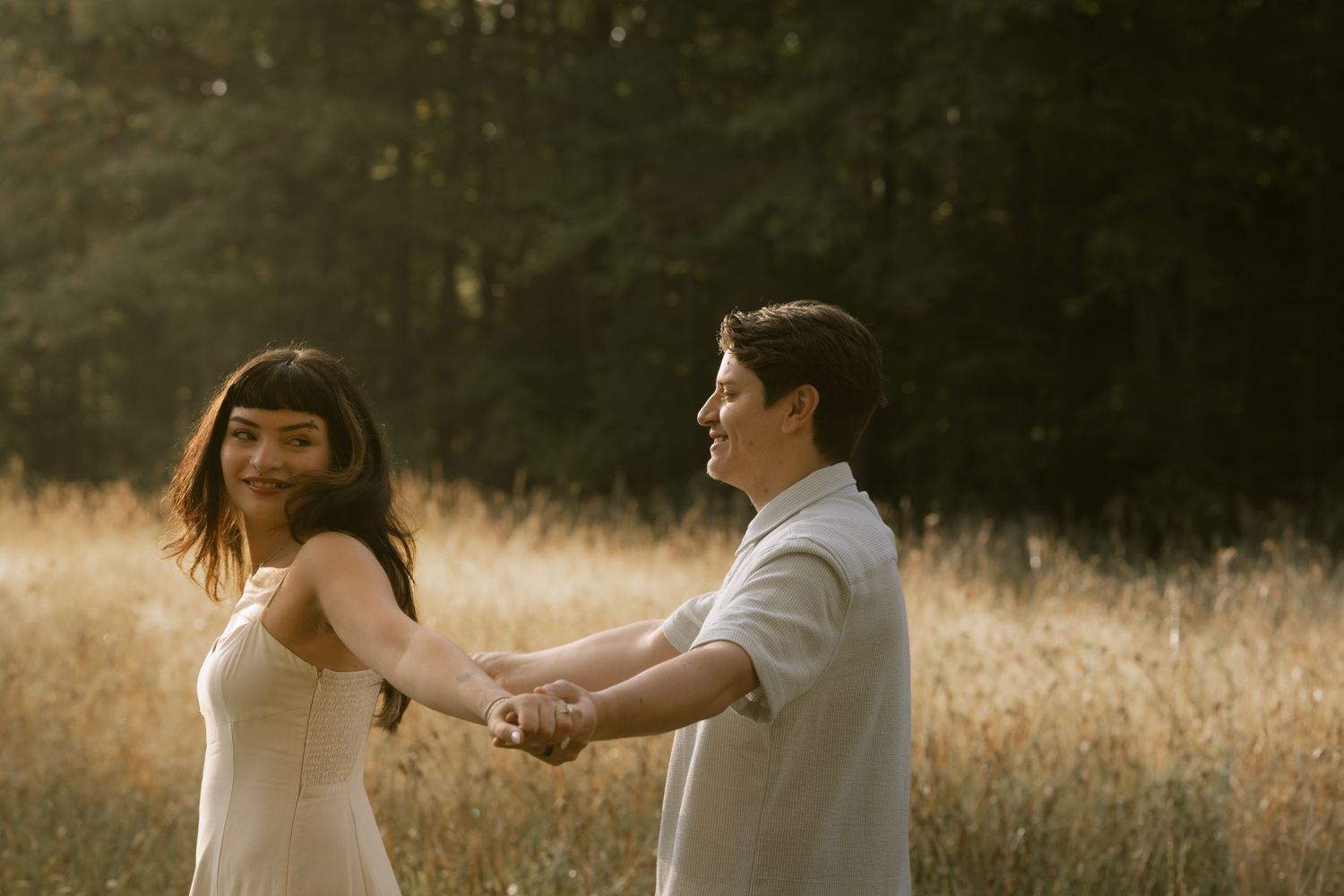 Couple in white outfits dancing in a golden field at sunset. Rochester NY authentic engagement photography