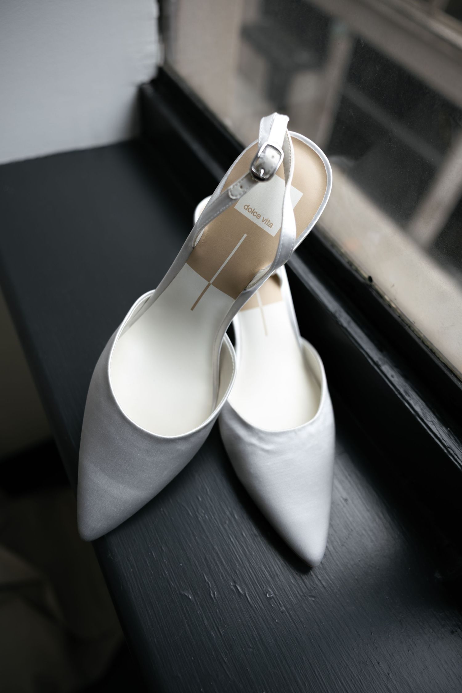 Elegant white pointed-toe bridal shoes on dark wooden surface.