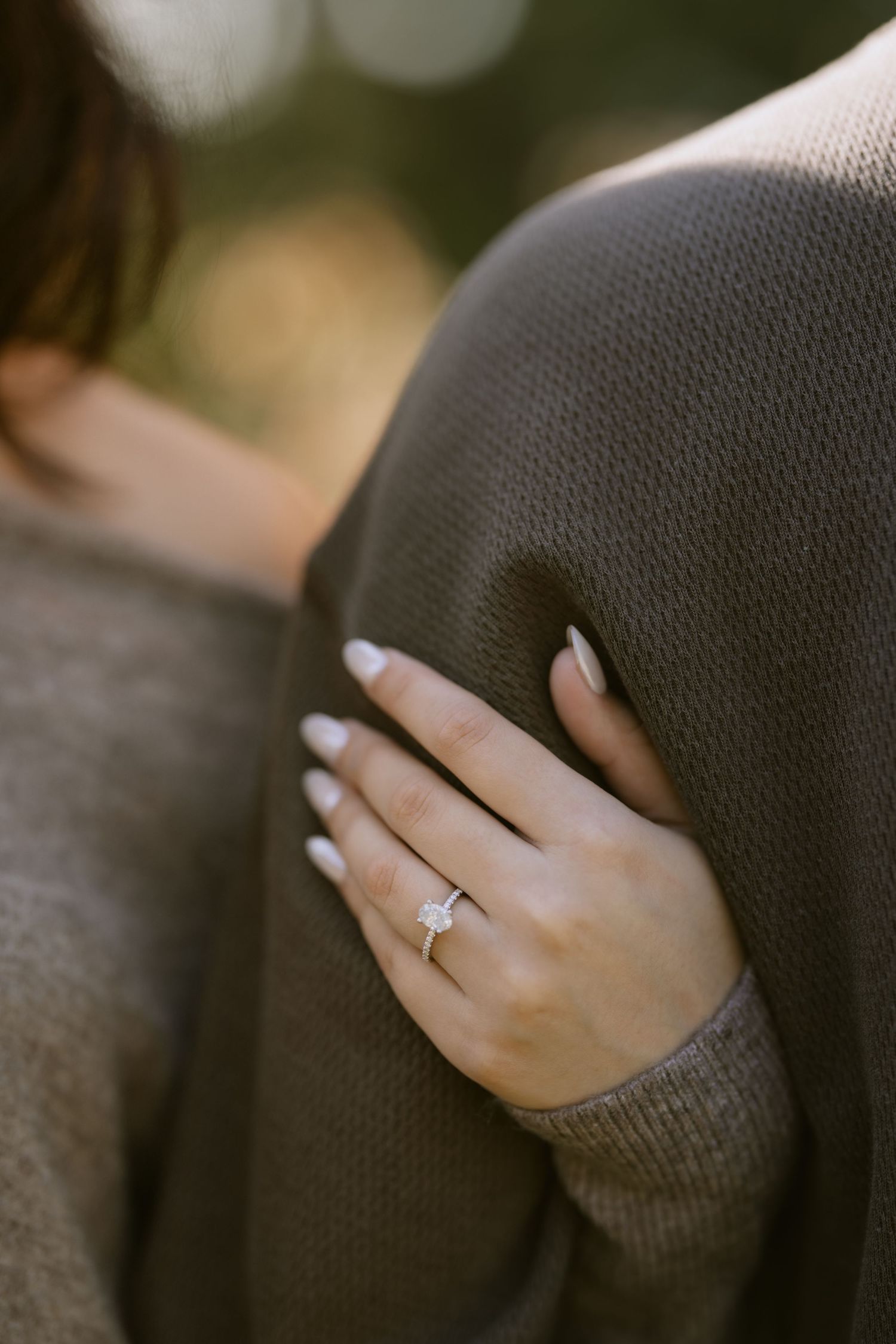 Close-up shot of a hand wearing an engagement ring against a gray sweater. Rochester NY documentary engagement photography