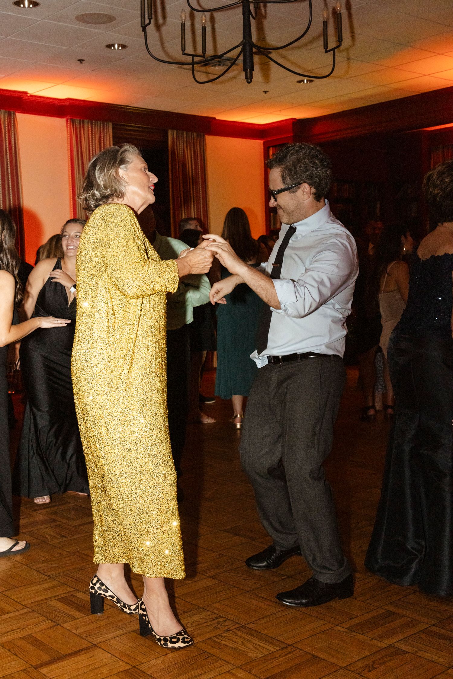 Formal event guests dancing, with one wearing a striking gold sequined dress. Rochester NY candid wedding photography