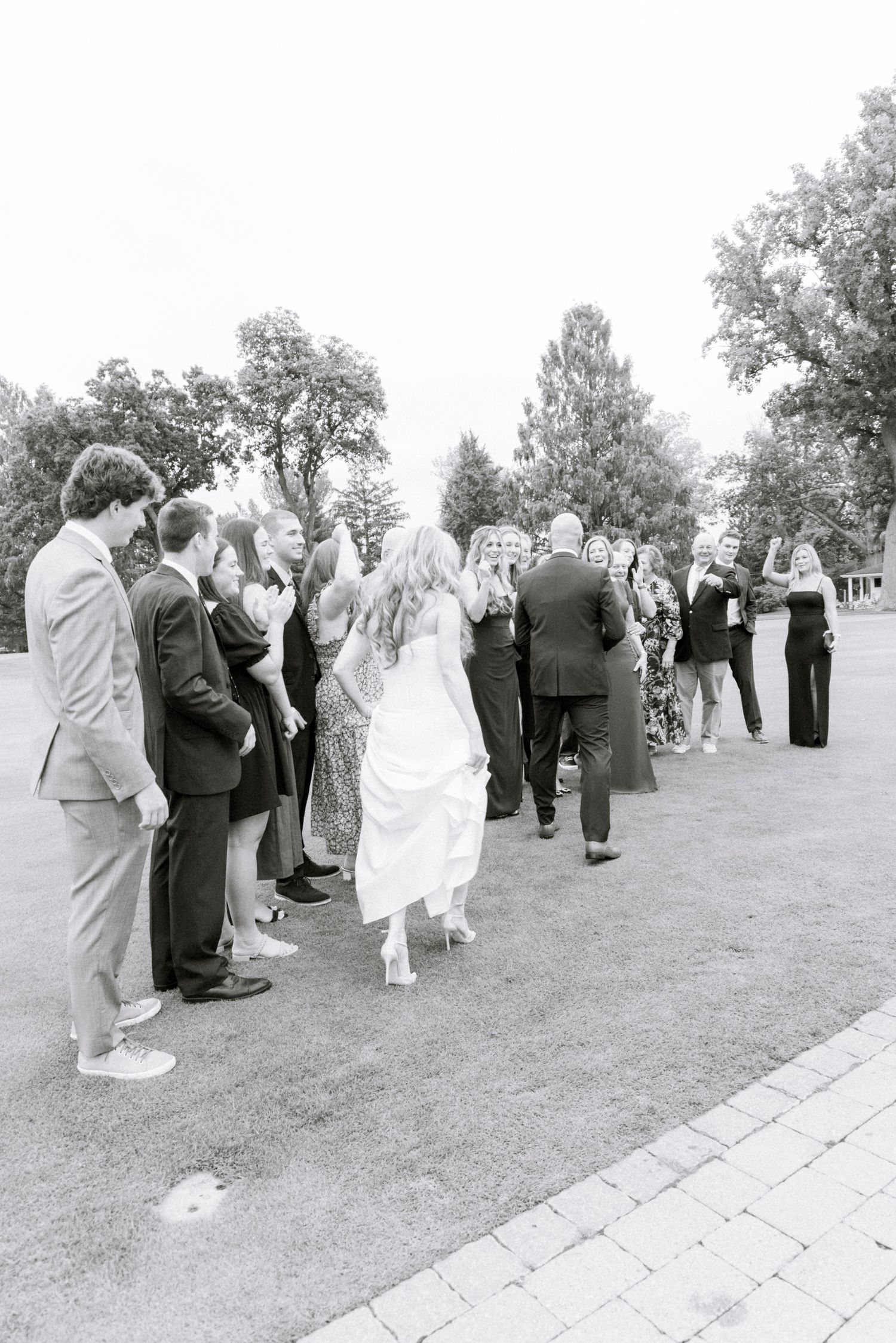 Wedding party and guests gathered on a grassy lawn during an outdoor ceremony. Rochester NY documentary wedding photography