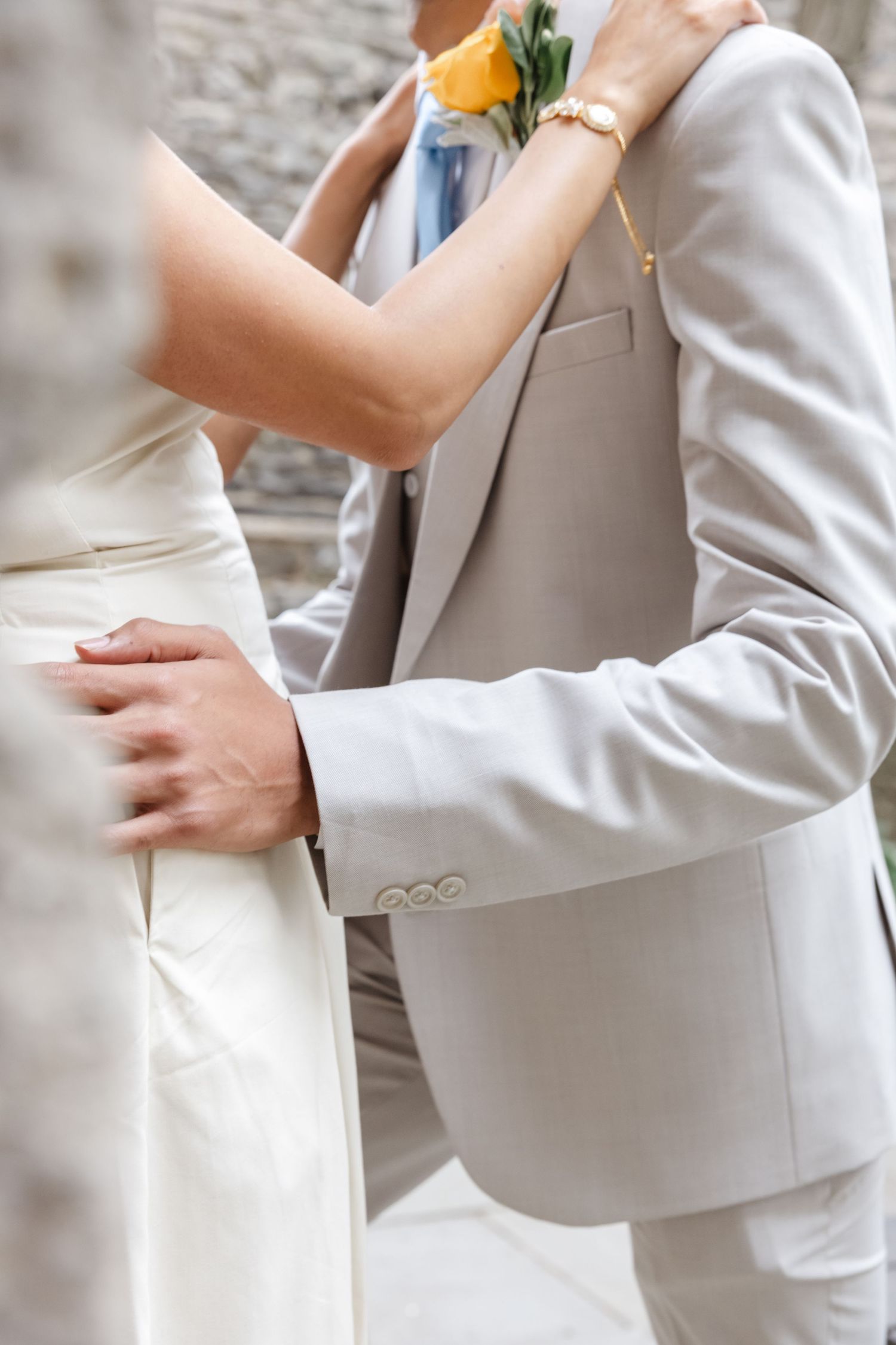 Close-up of formal attire showing a light colored suit jacket and white dress with yellow boutonniere.  St. Josephs park wedding photographe