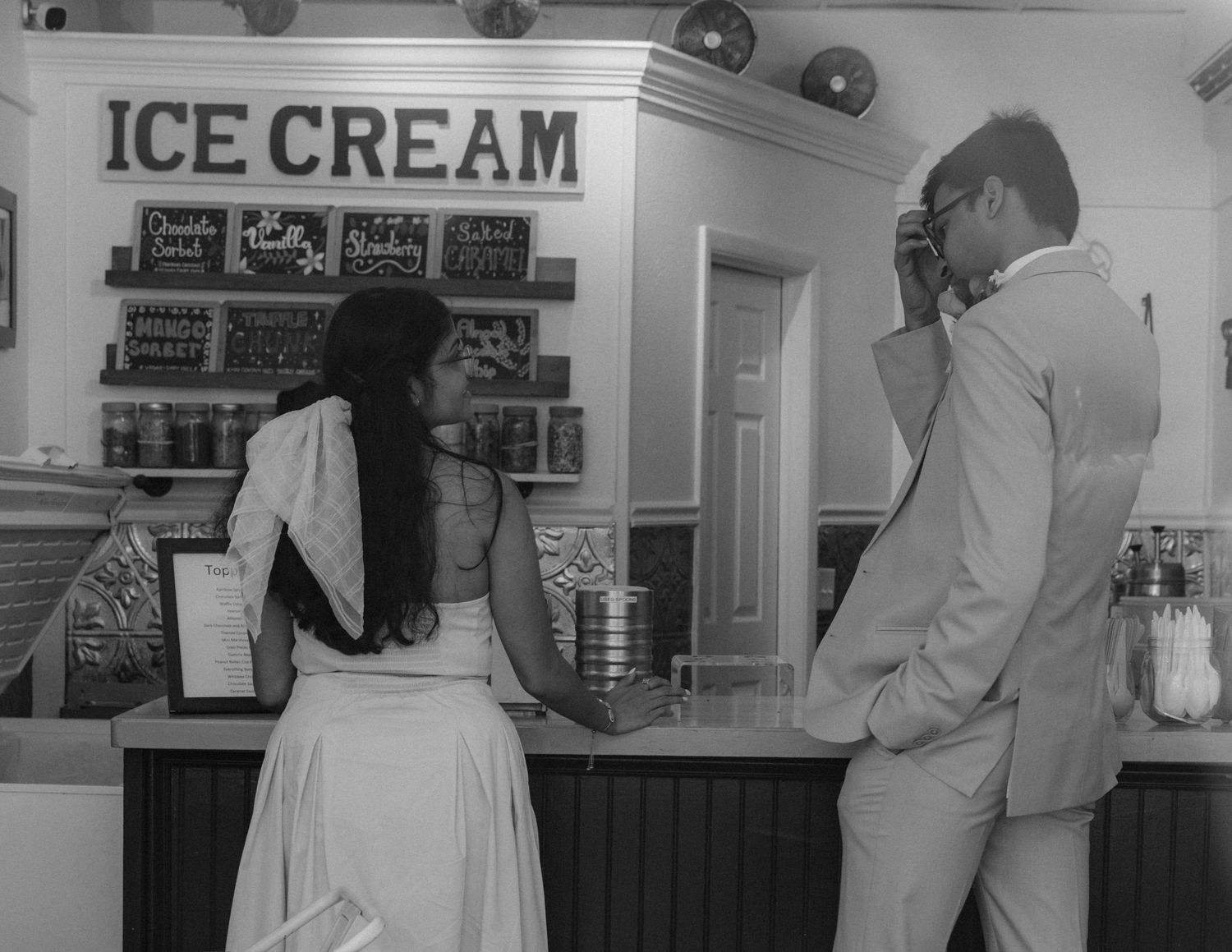 A black and white photo of two people at an ice cream counter with menu boards visible.  Fun elopement photography Rochester NY