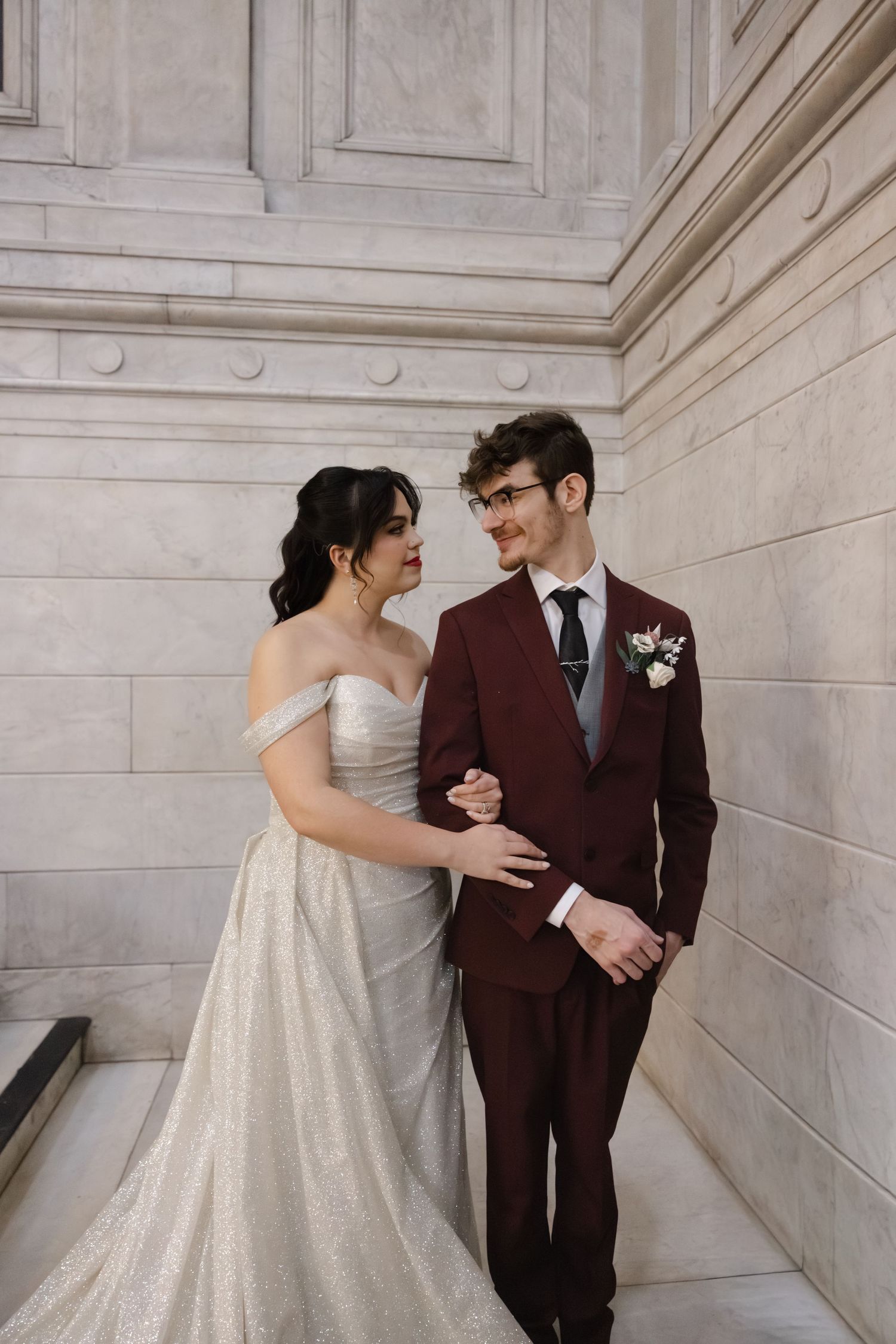 A couple shares an intimate moment in a grand marble corridor with classical architectural elements.