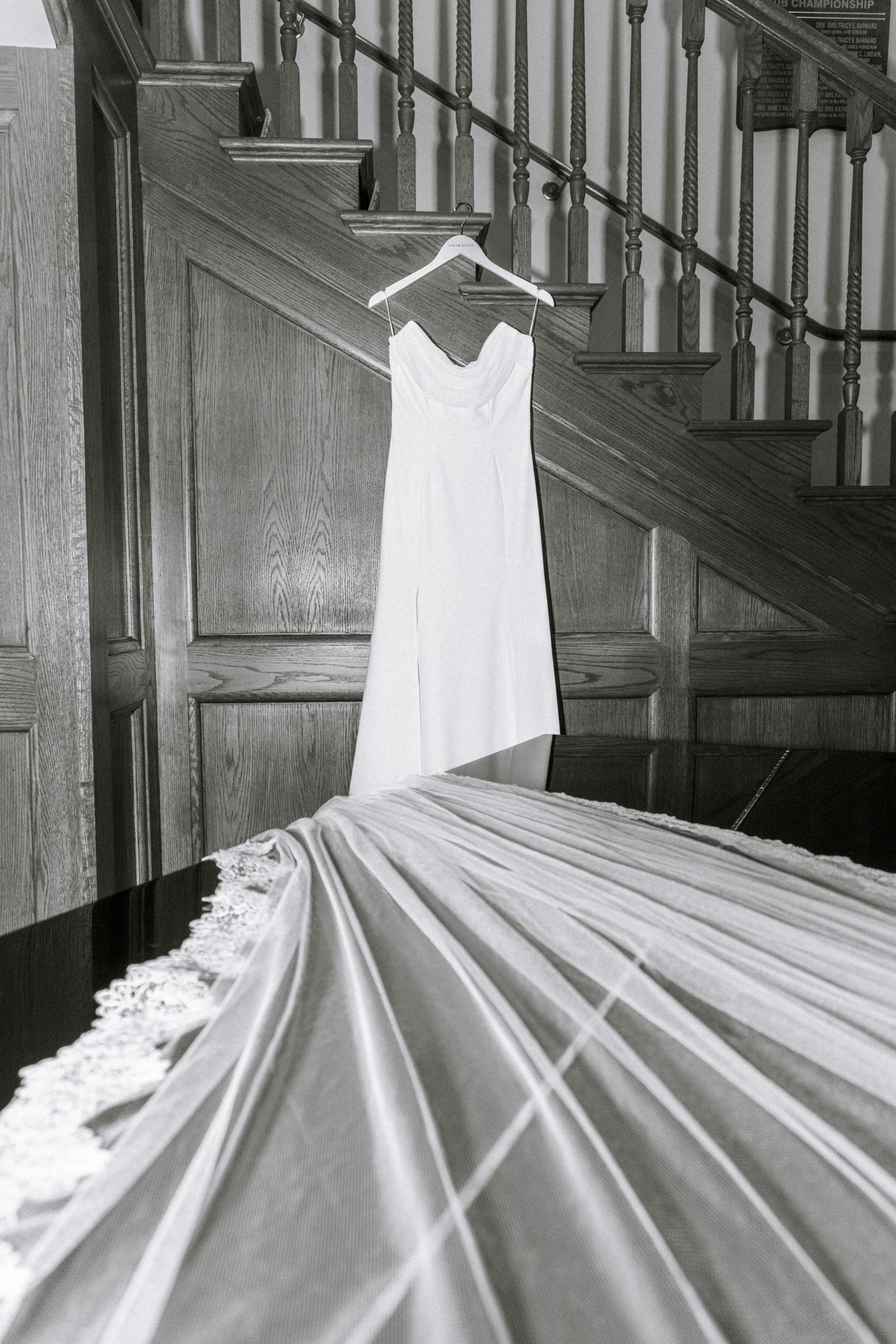A white wedding dress hangs elegantly on wooden stairs in dramatic black and white.Rochester NY documentary wedding photography