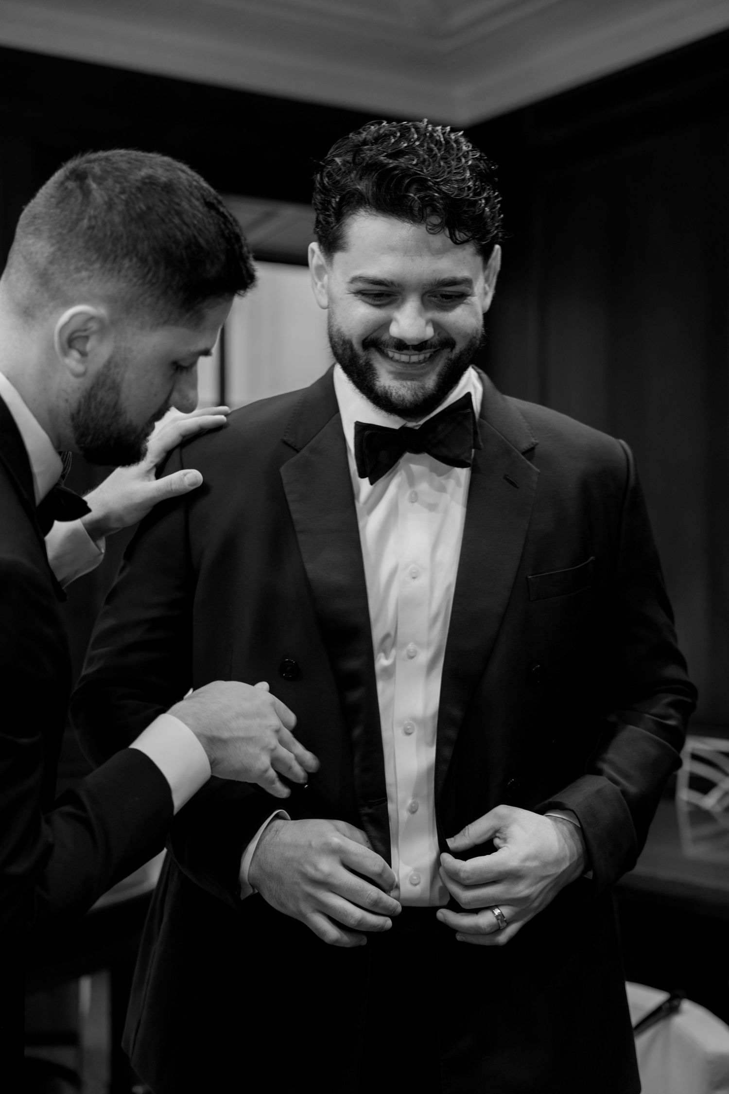 Men in suits sharing a lighthearted moment during formal event preparations.